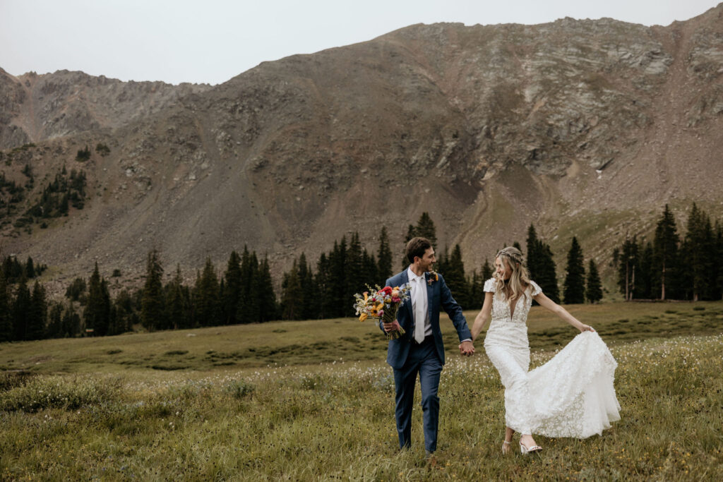 bride and groom walk through field under mountainside during colorado micro wedding.