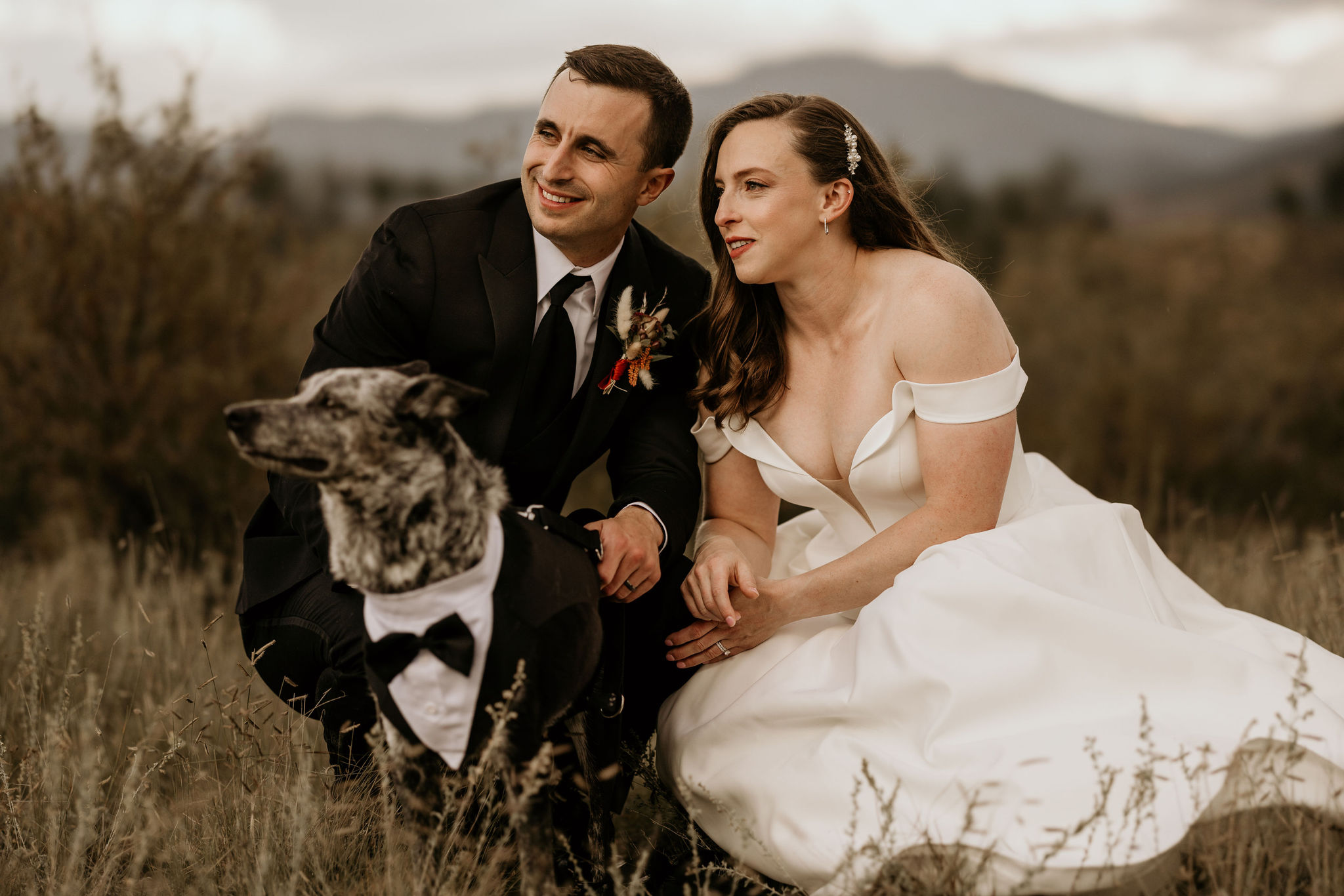 bride and groom pose with dog during wedding portraits.