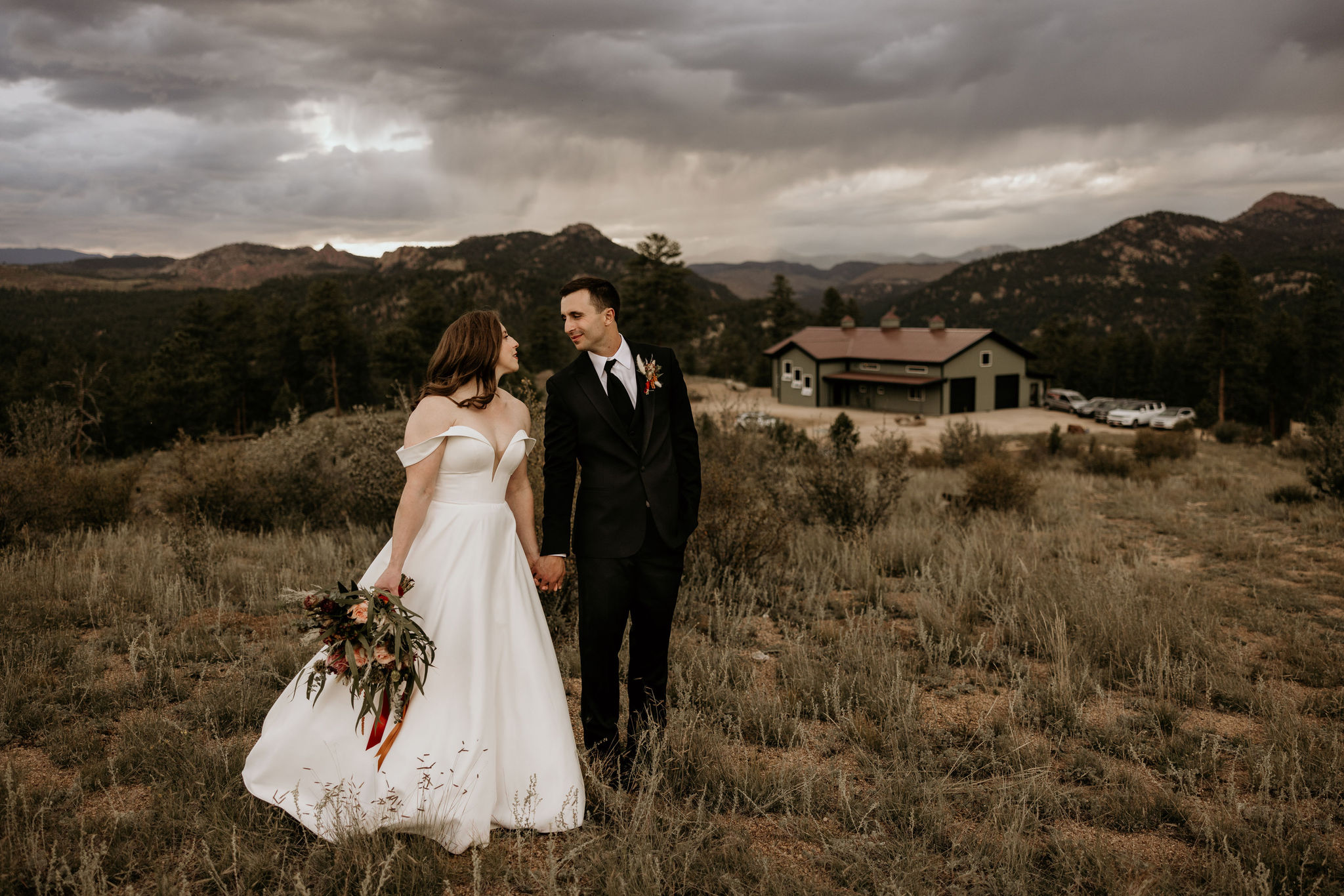 bride and groom hold hands and smile at each other with colorado wedding venue in the back.