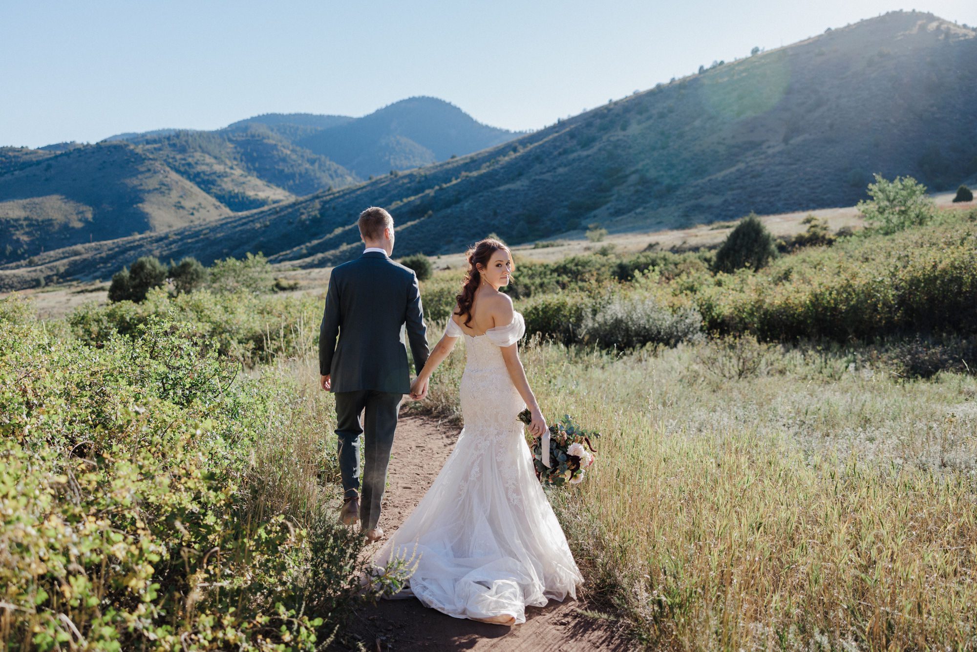 bride and groom walk along path at Red Rocks Park for their elopement with flowers from a vendor