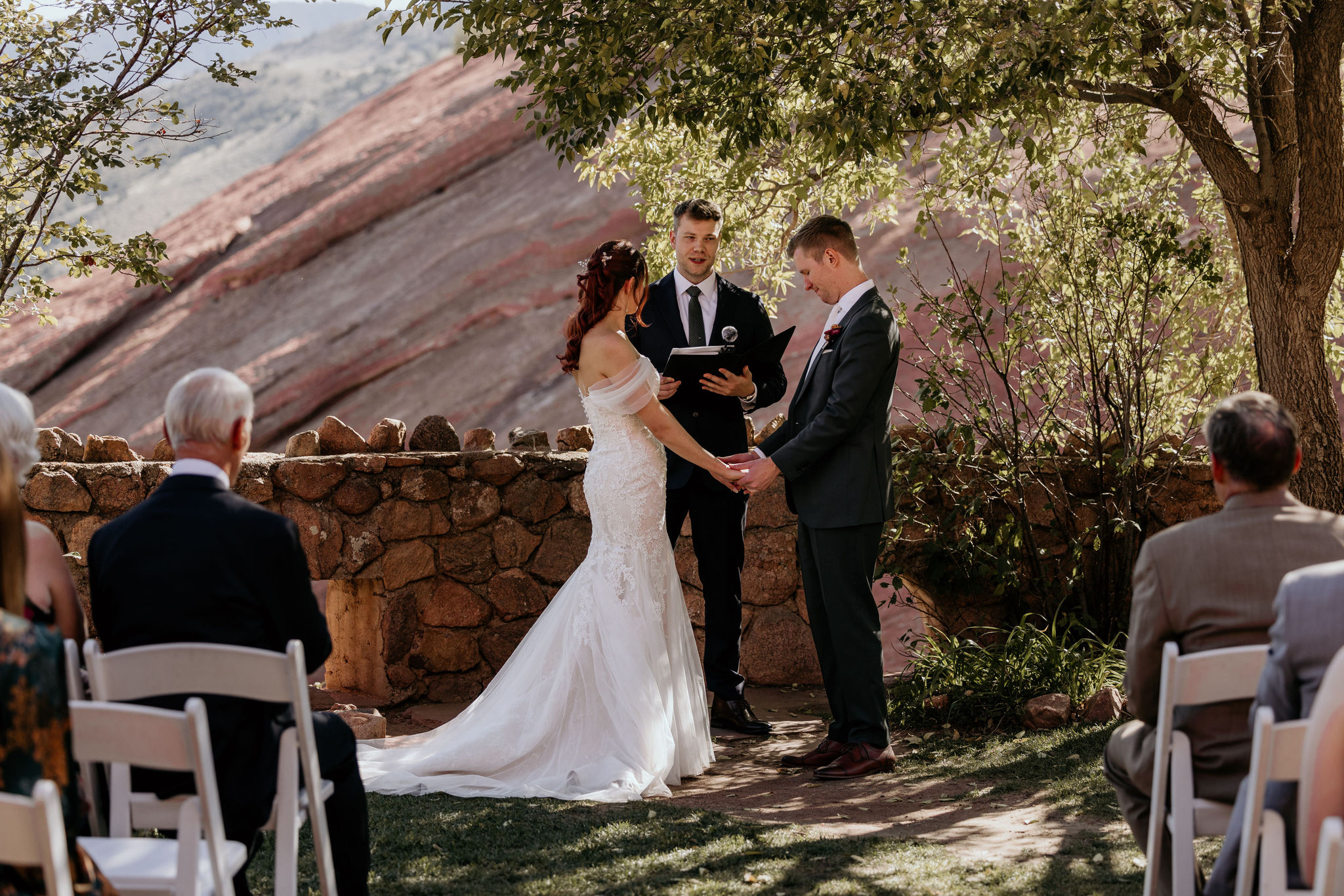 bride and groom stand with officiant during red rocks wedding ceremony.