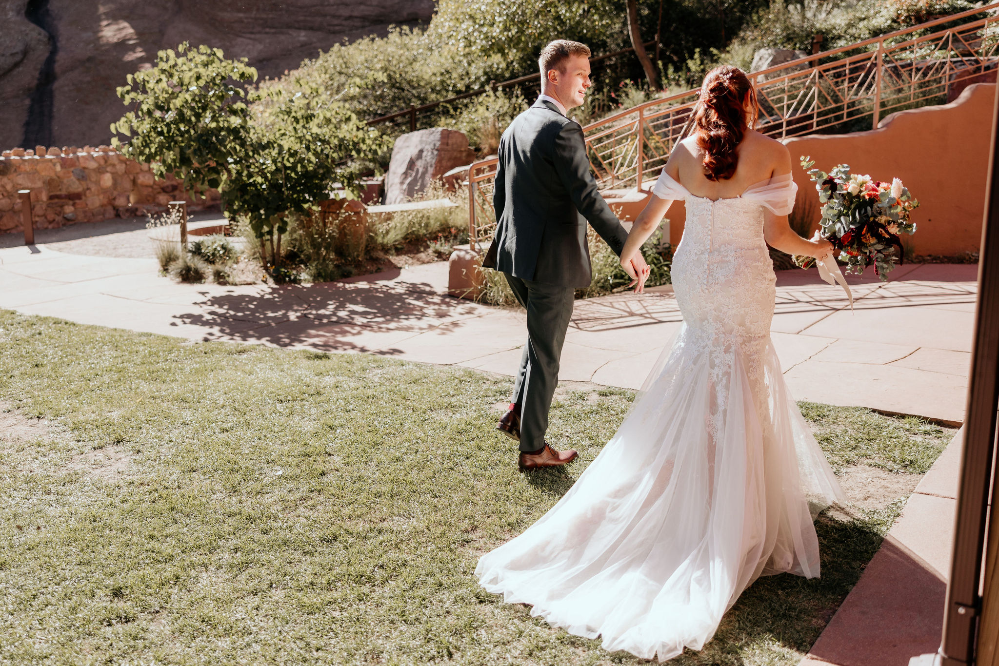 bride and groom hold hands and walk at red rocks trading post.