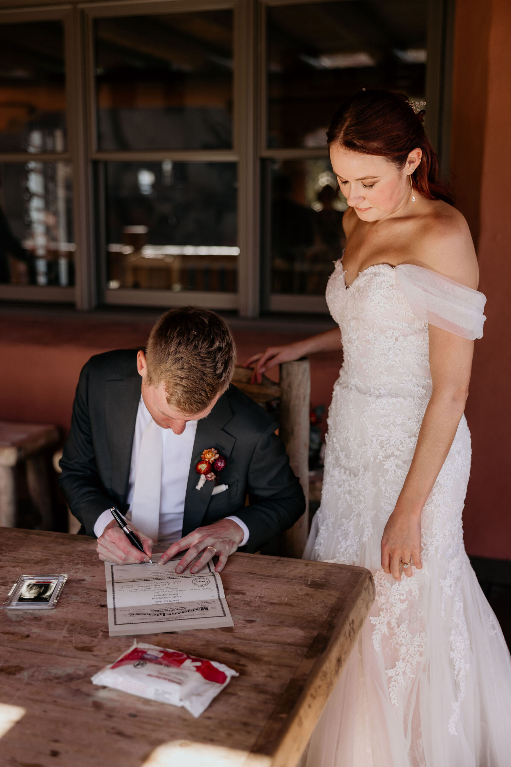 bride stands behind groom while he signs the colorado marriage certificate