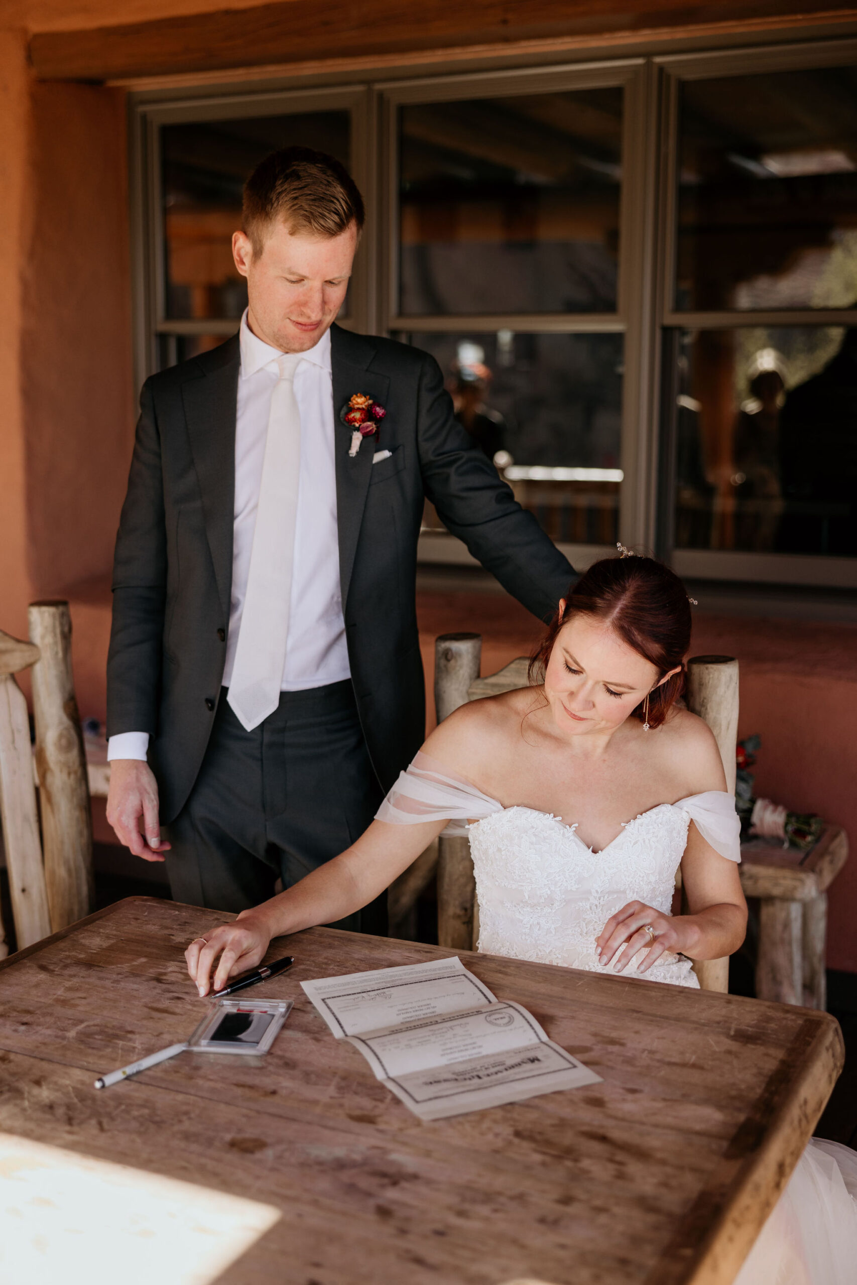 groom stands behind bride as she signs the colorado marriage certificate.