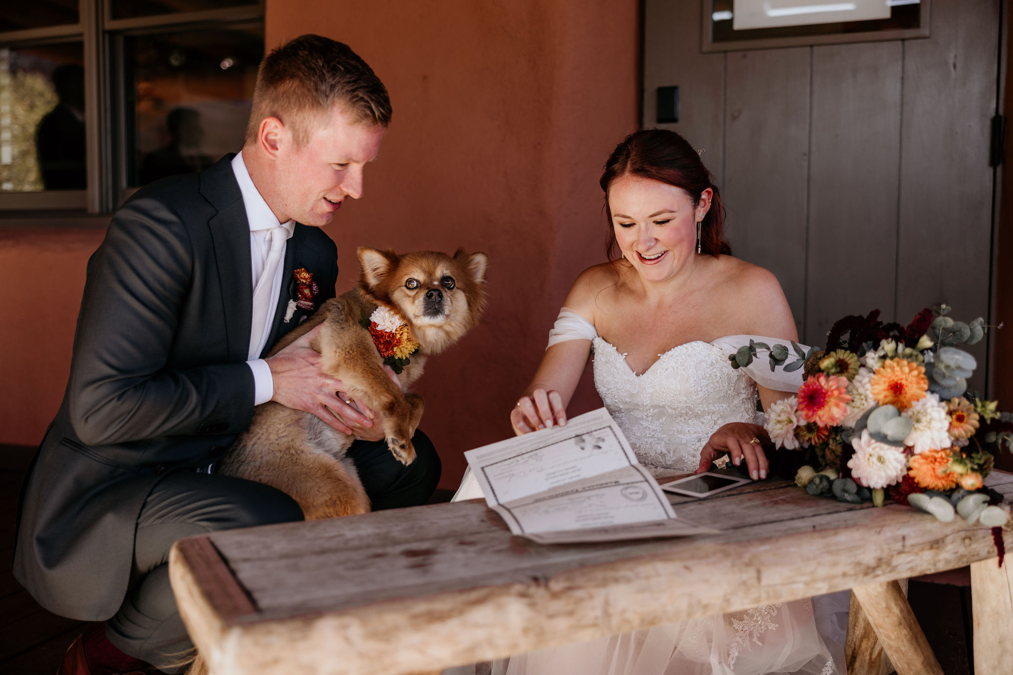 groom holds dog as bride grabs marriage certificate.