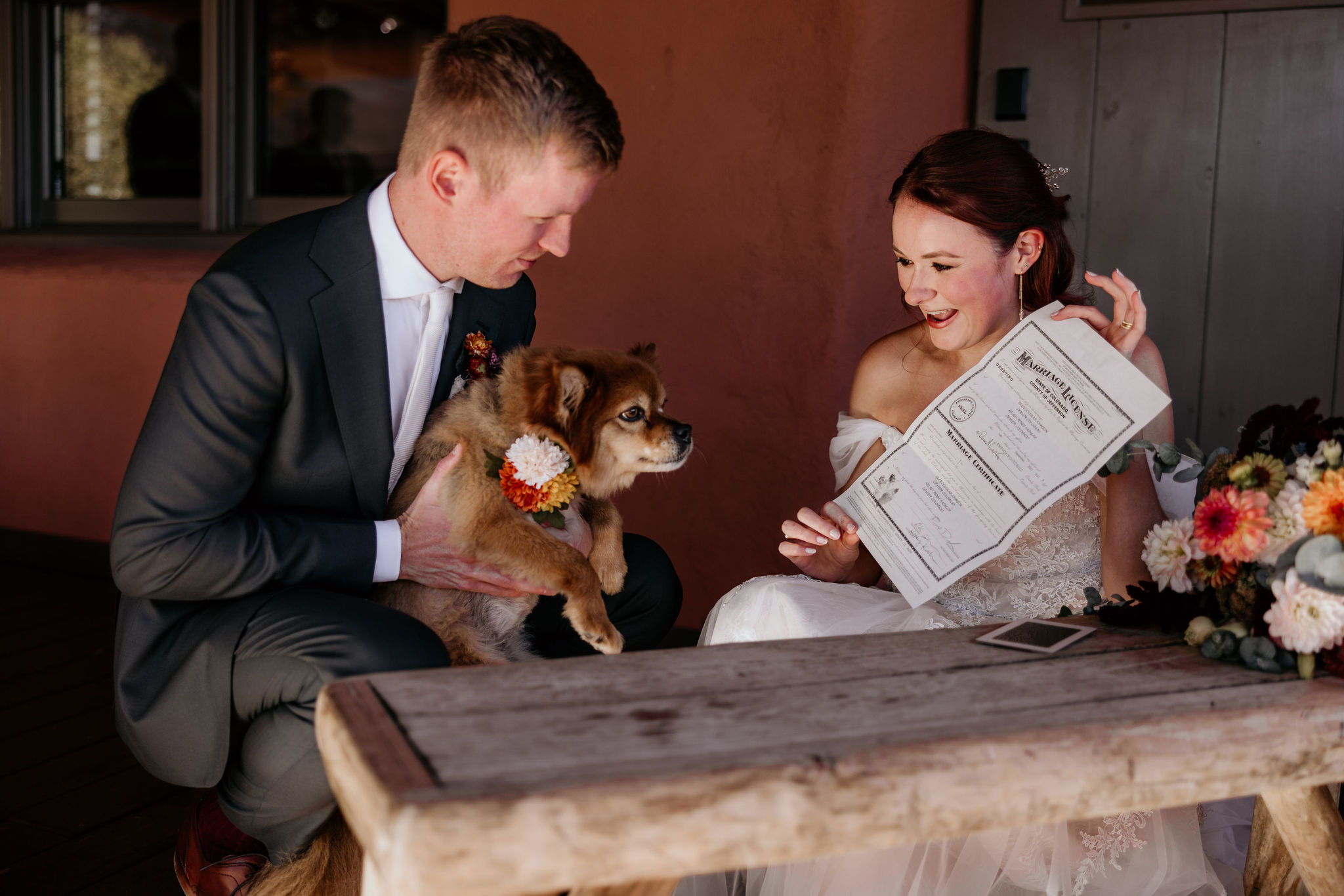 groom holds dog as bride shows dog the marriage certificate.