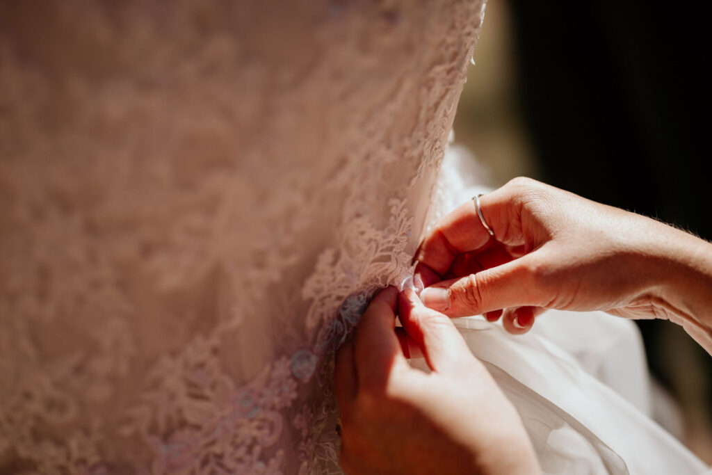 close up image of hands helping a bride with her wedding dress.