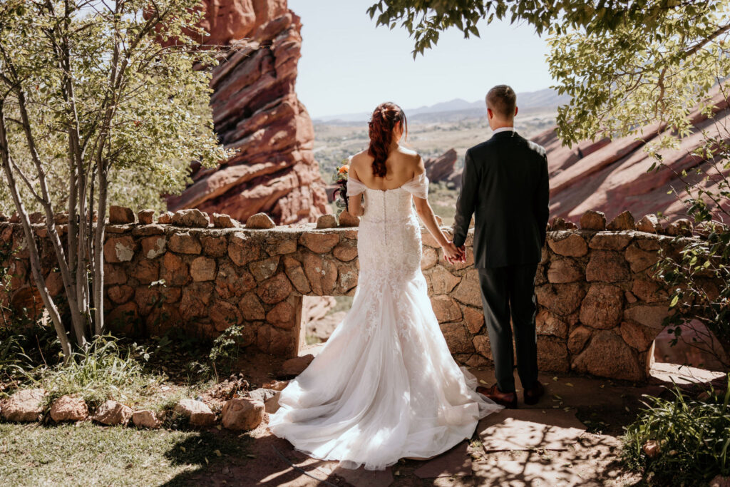 bride and groom hold hands and look out at red rocks park and amphitheatre.
