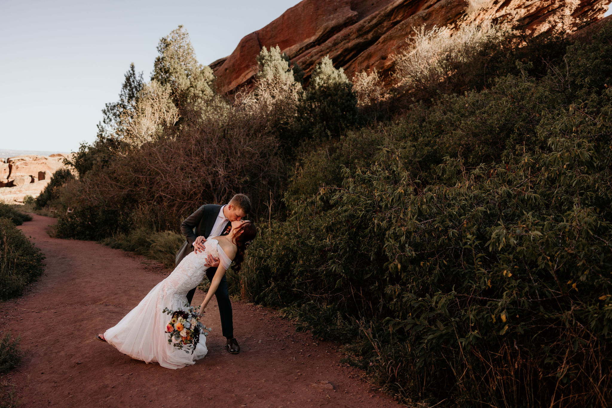 groom dips bride during wedding photos at red rocks park and amphitheatre.