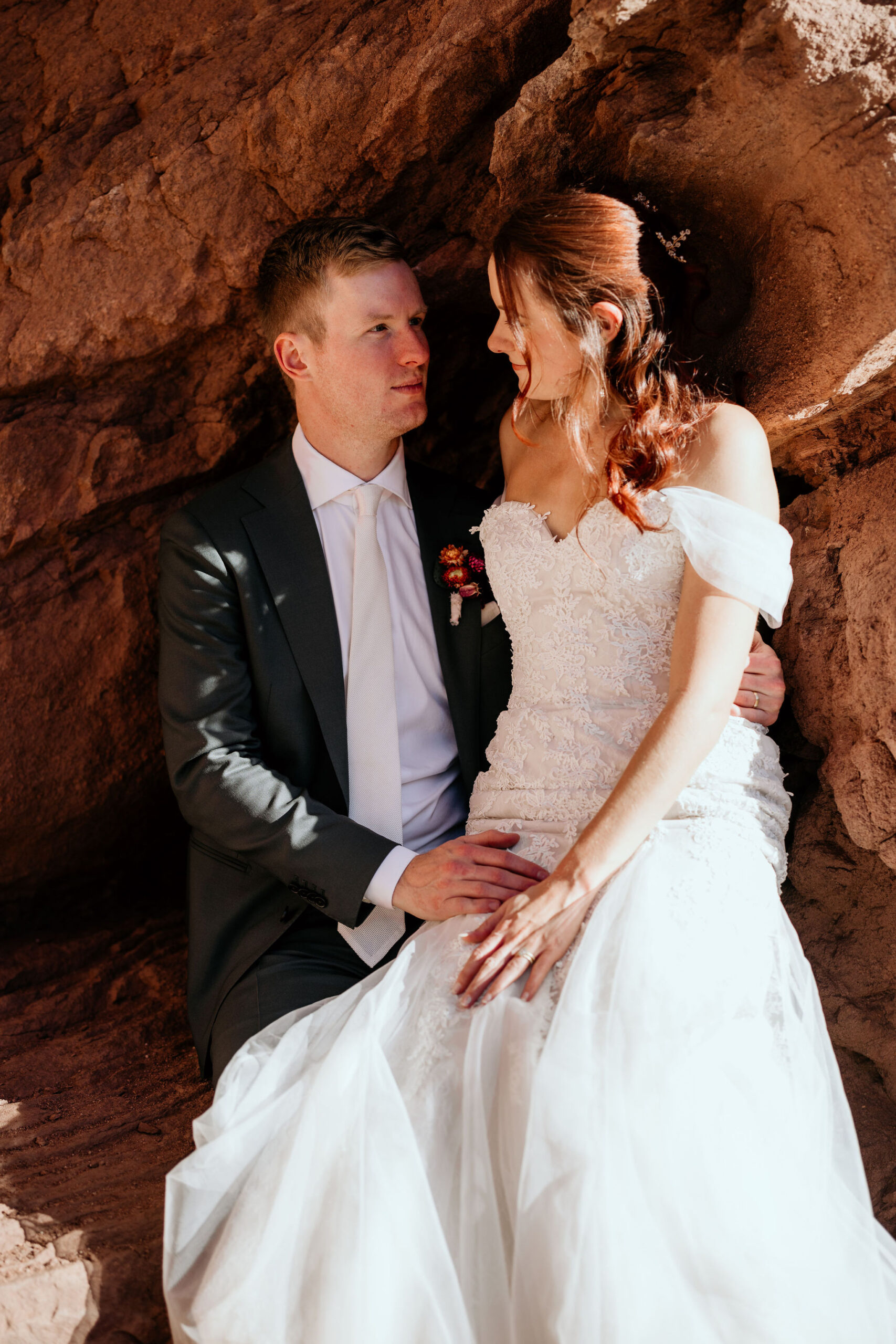 bride and groom sit on red rocks during colorado elopement wedding.
