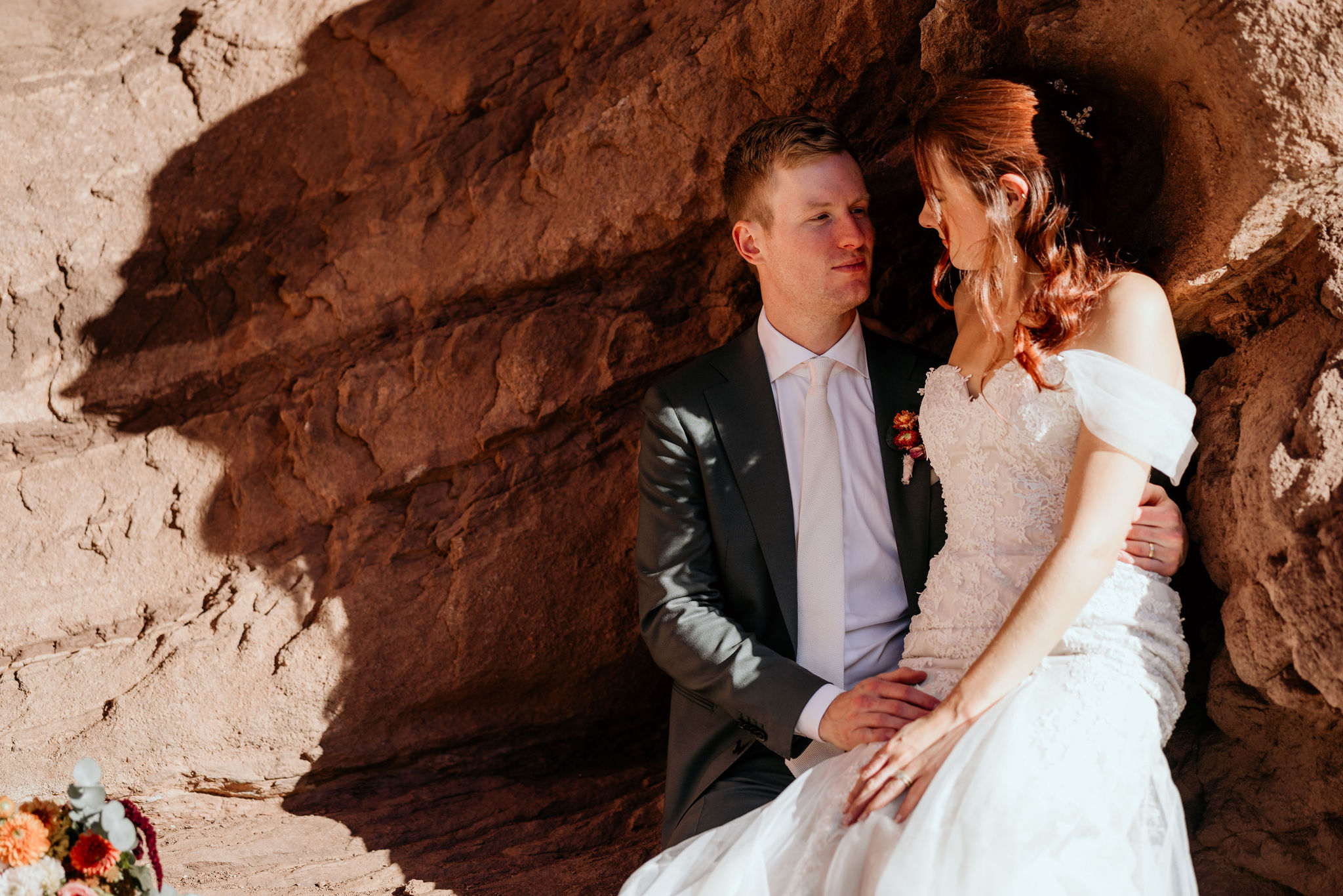 bride and groom sit on red rock during colorado wedding portraits.