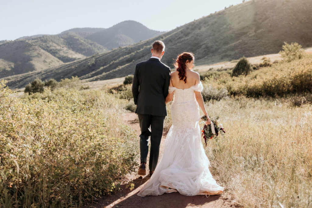 bride and groom hold hands and walk along trail at red rocks.