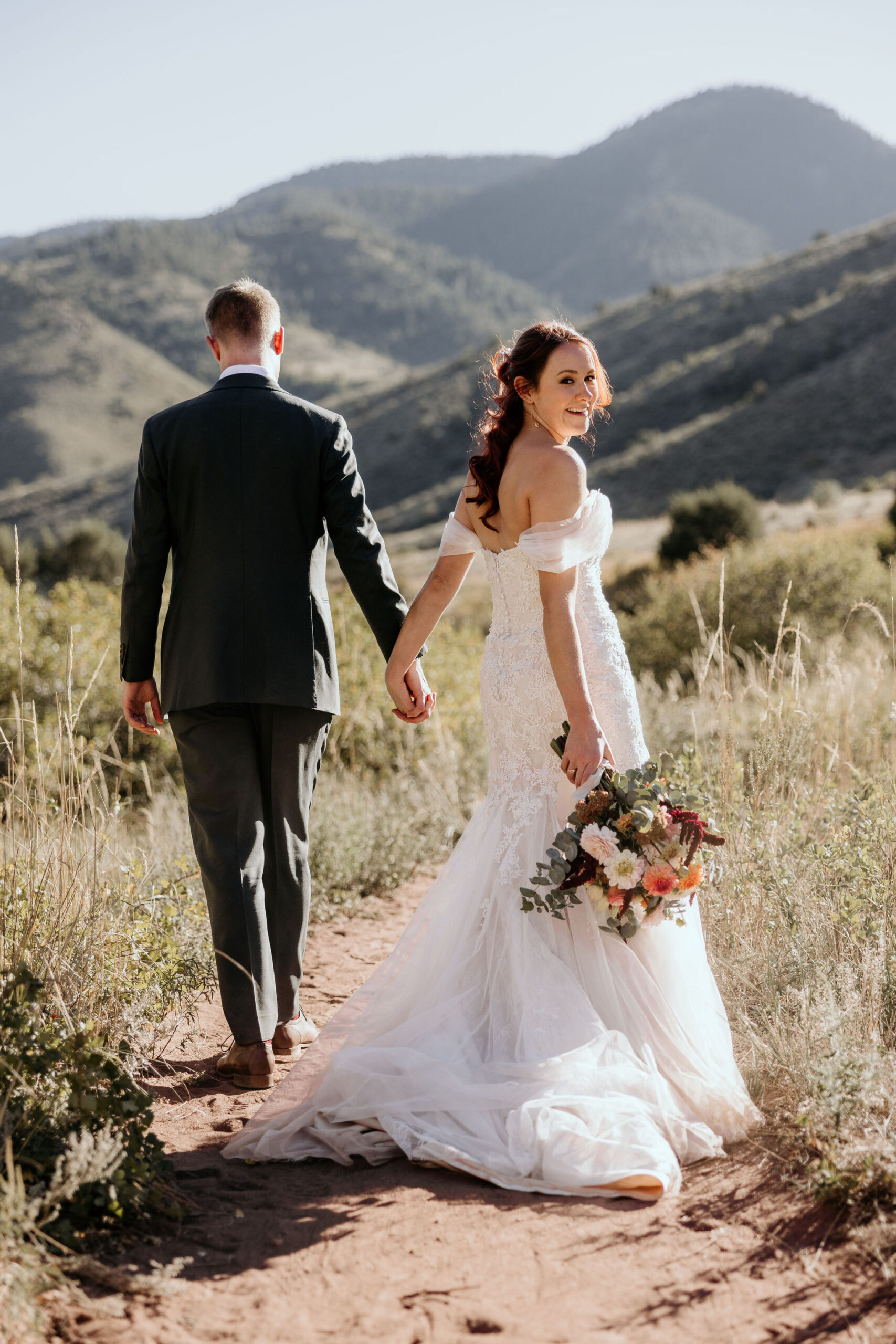 bride and groom walk along trail at red rocks park and amphitheatre during colorado micro wedding.
