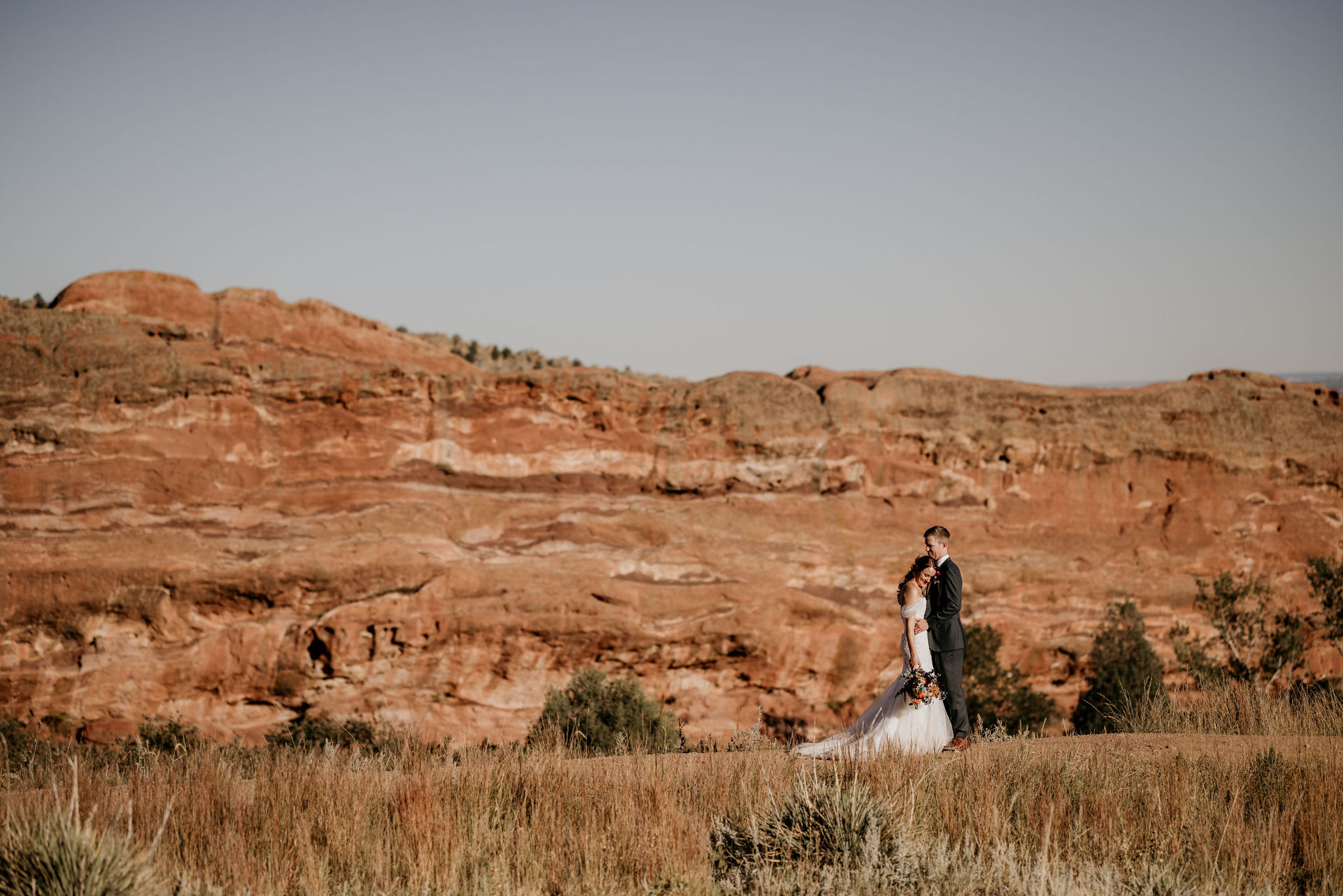 bride and groom walk down trail at red rocks during their wedding portraits.