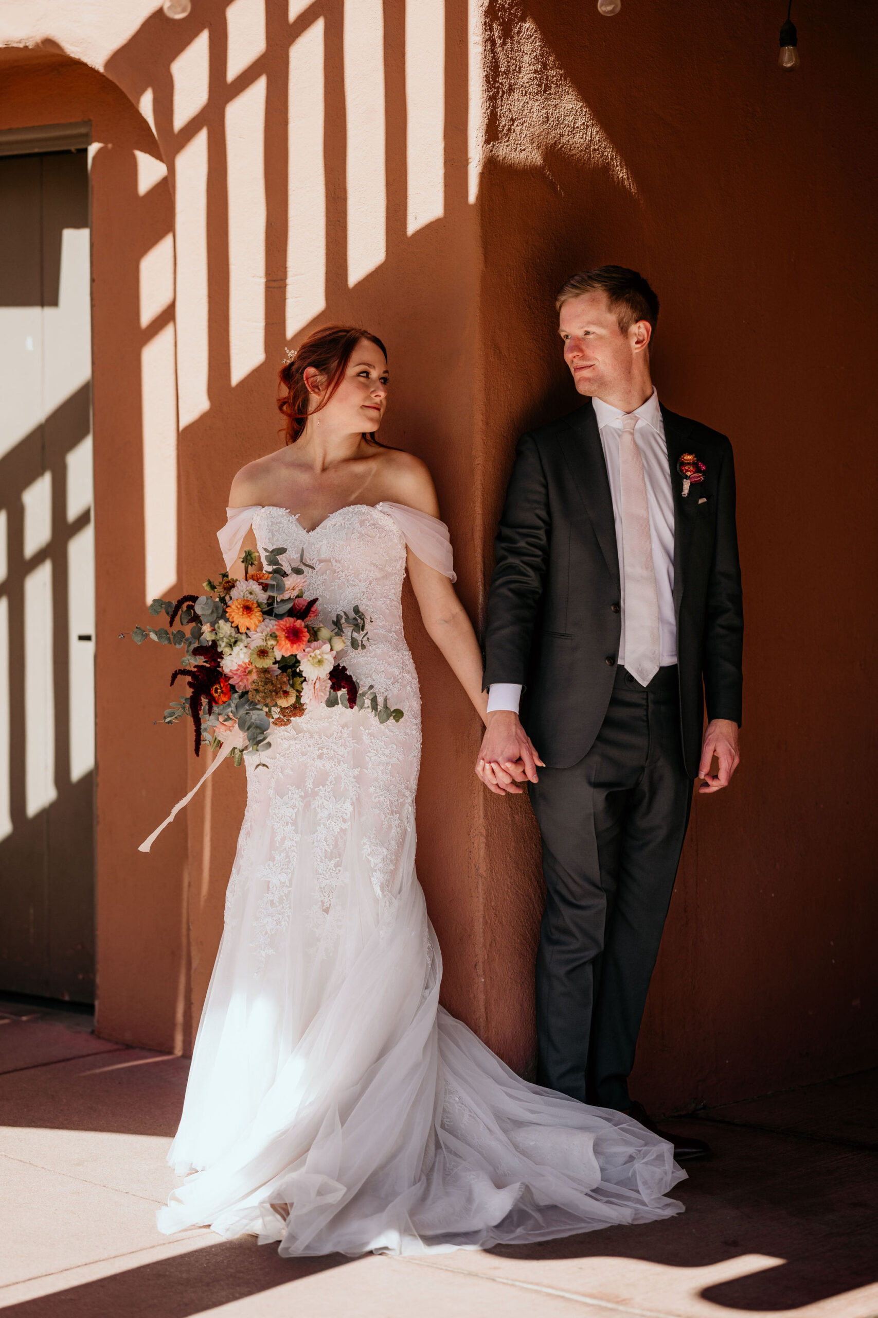 bride and groom hold hands at corner of red rocks trading post and smile.