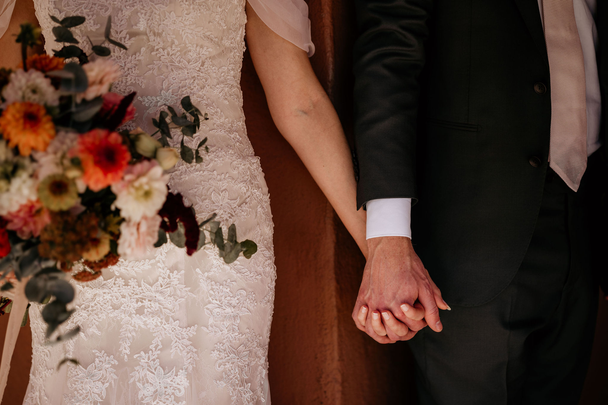 bride holds wedding bouquet and her other hand holds the grooms hand.