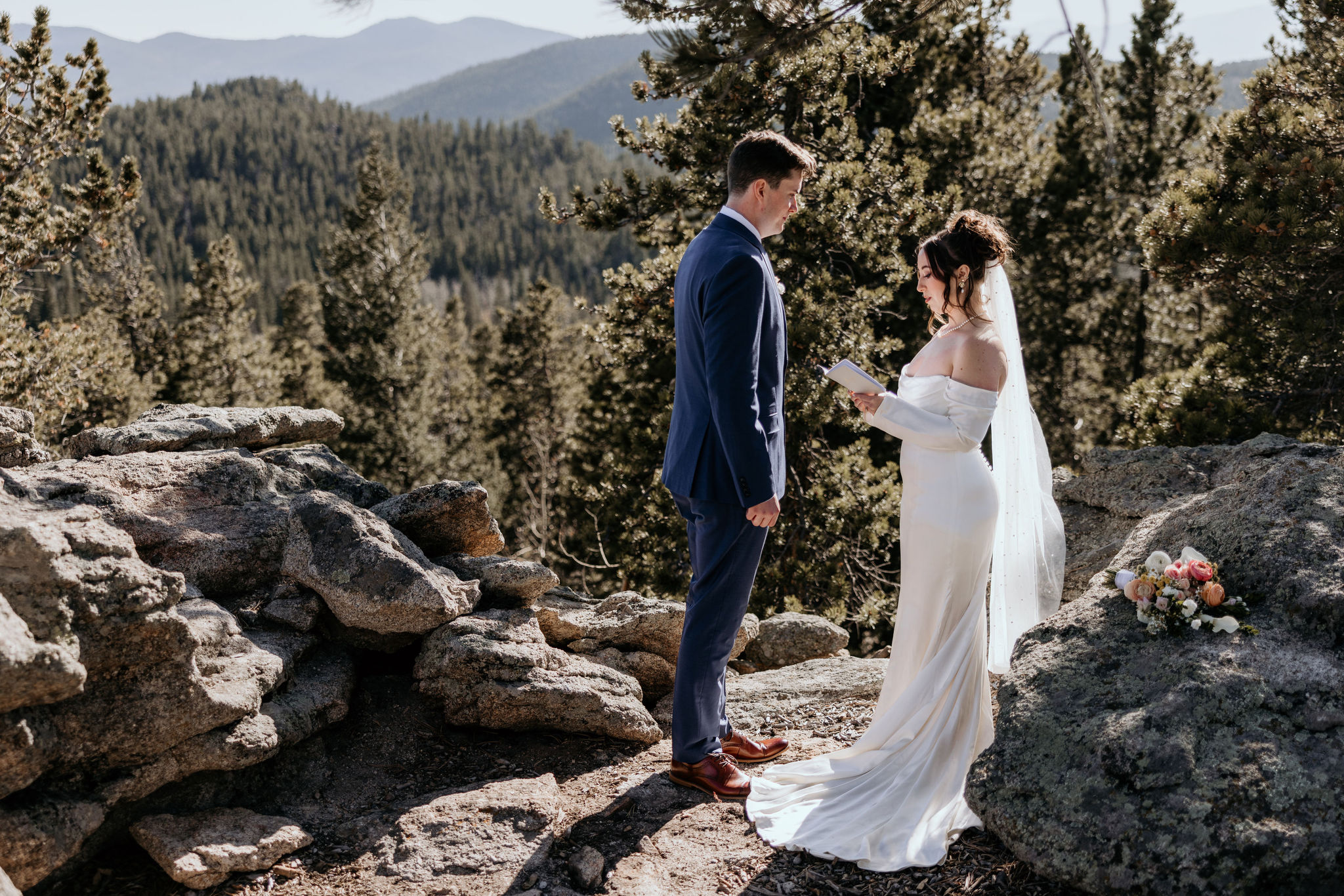 bride and groom stand on rock ledge in the colorado mountains during airbnb wedding.