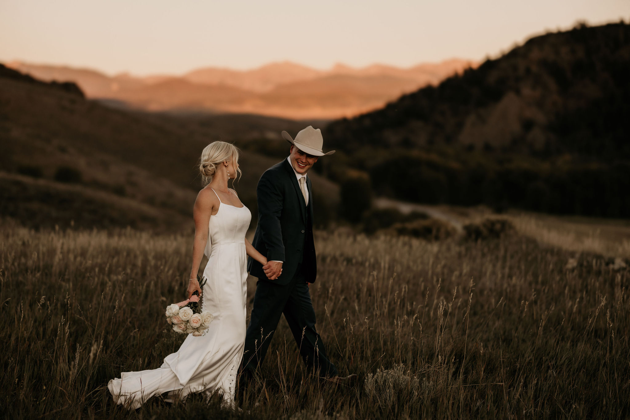bride and groom hold hands and walk through field during colorado elopement day.