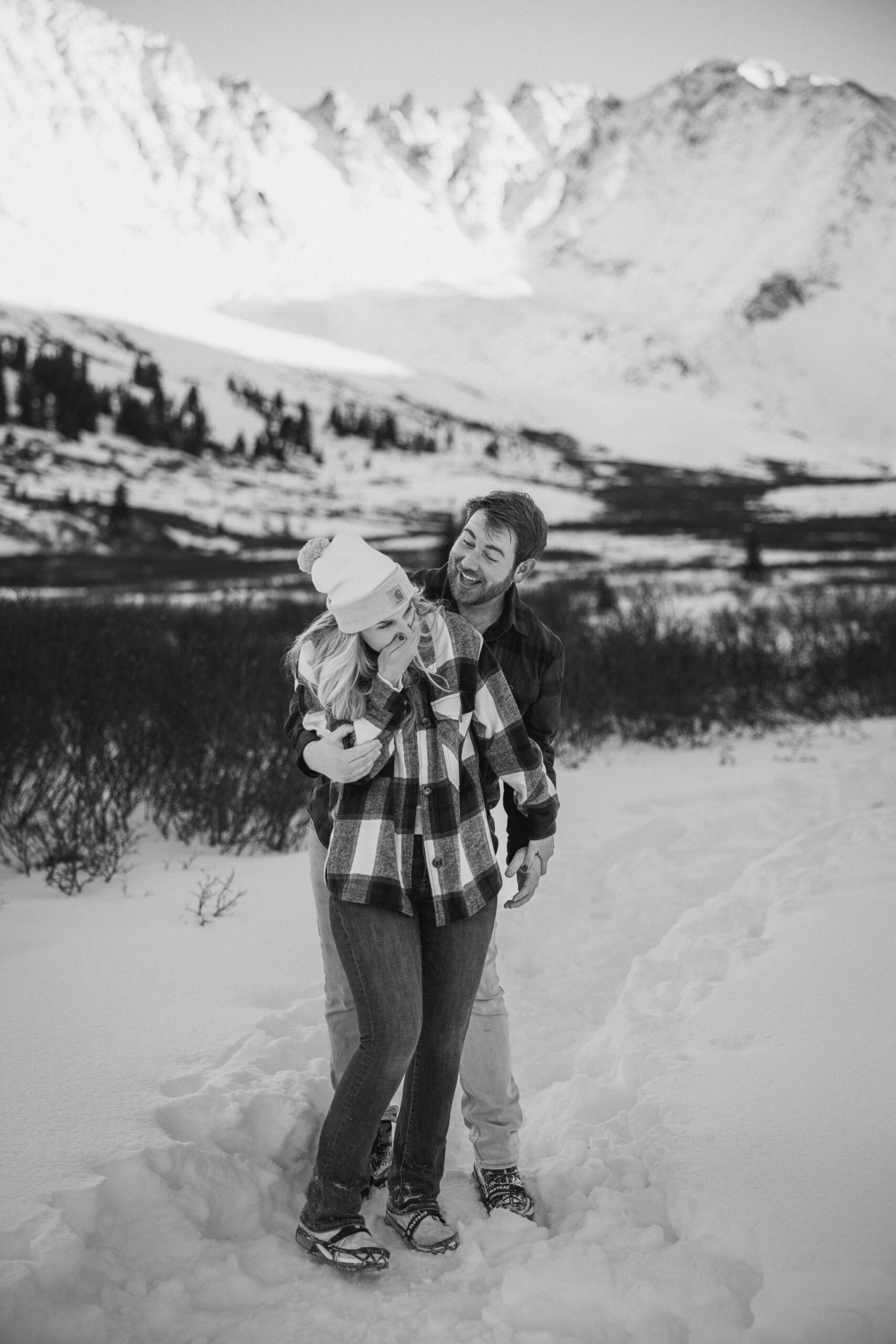 engaged couple laugh while hiking a snowy winter trail in colorado