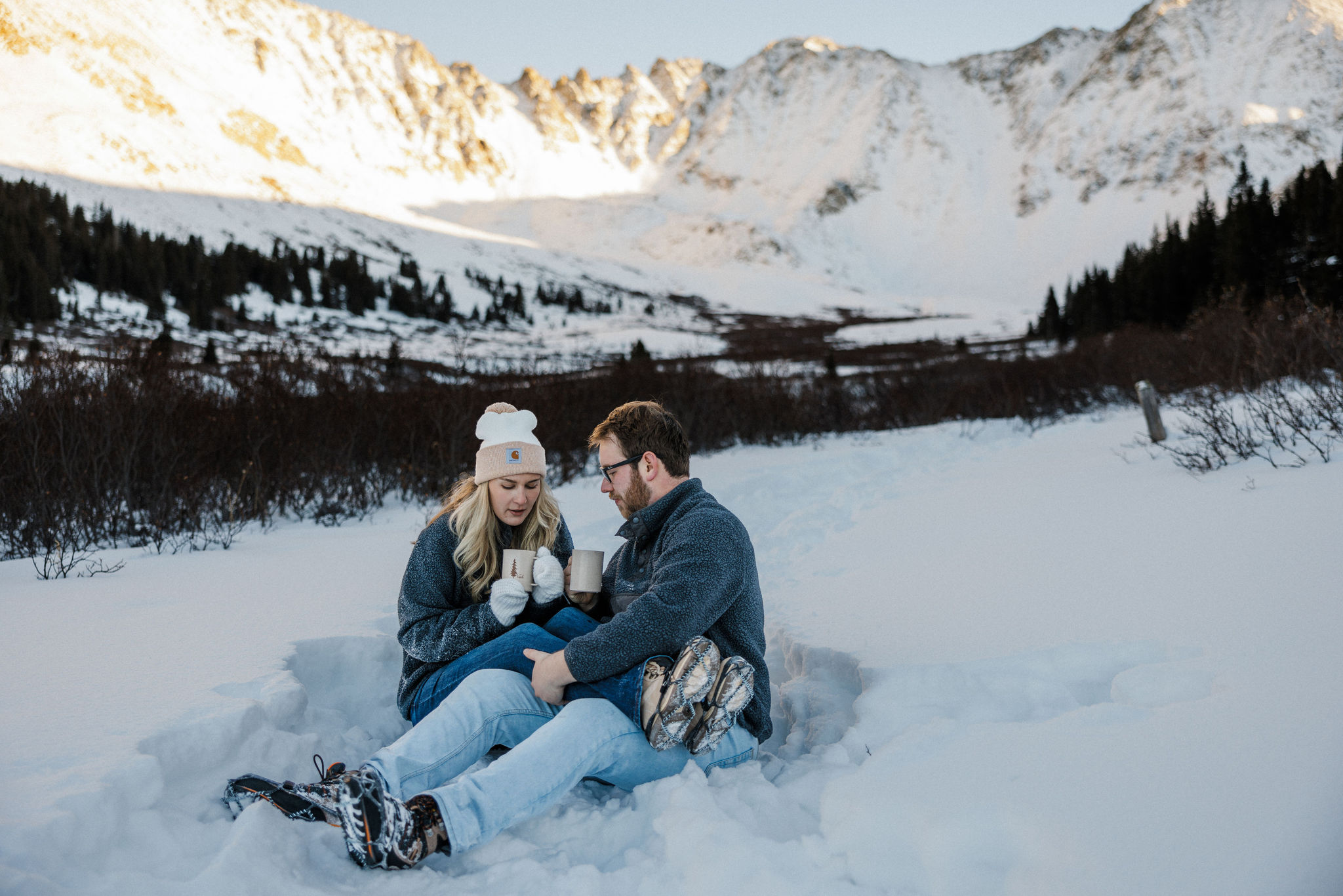 engaged couple enjoys a cup of coffee while taking winter engagement photos.