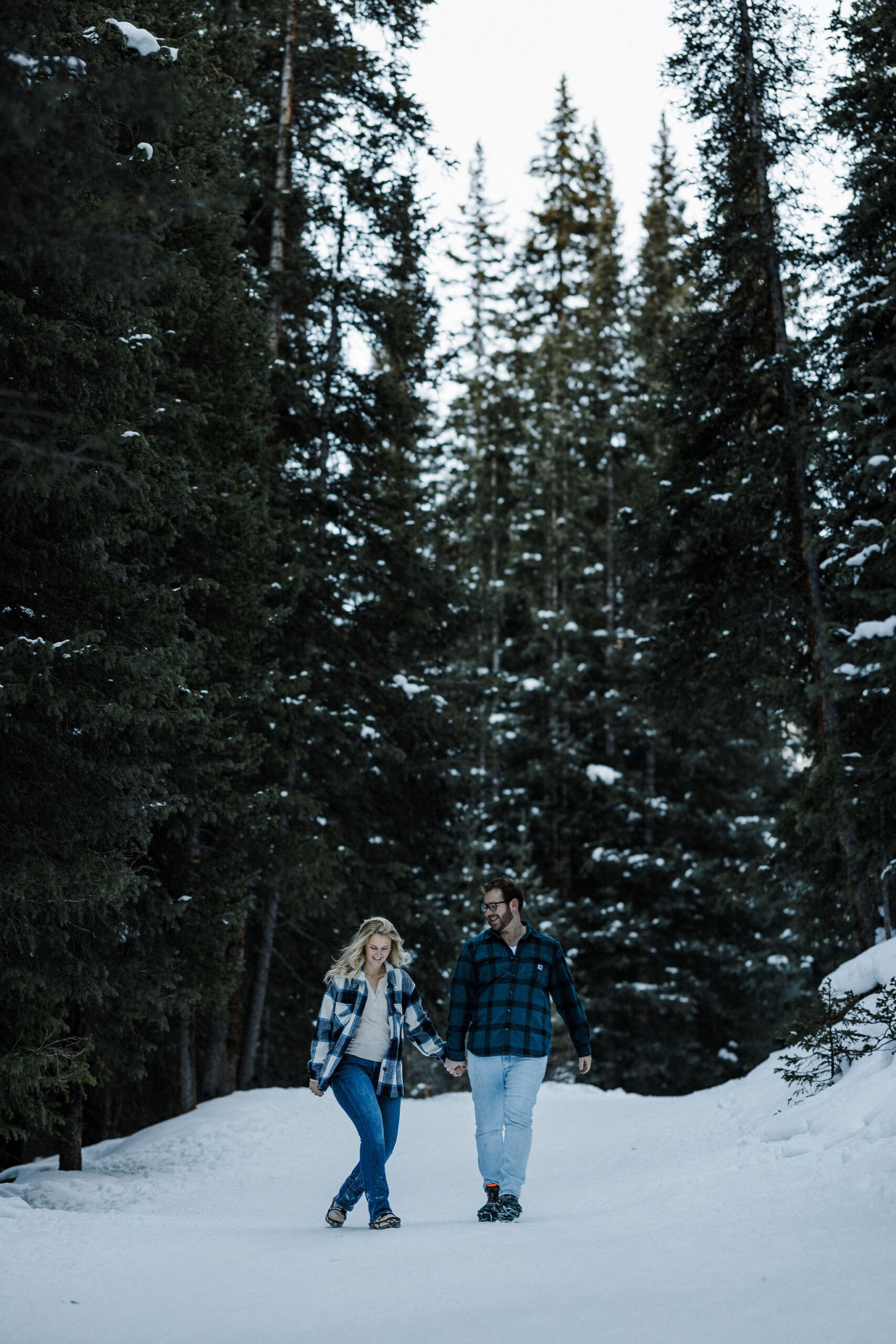 engaged couple walks down snowy trail in the colorado winter