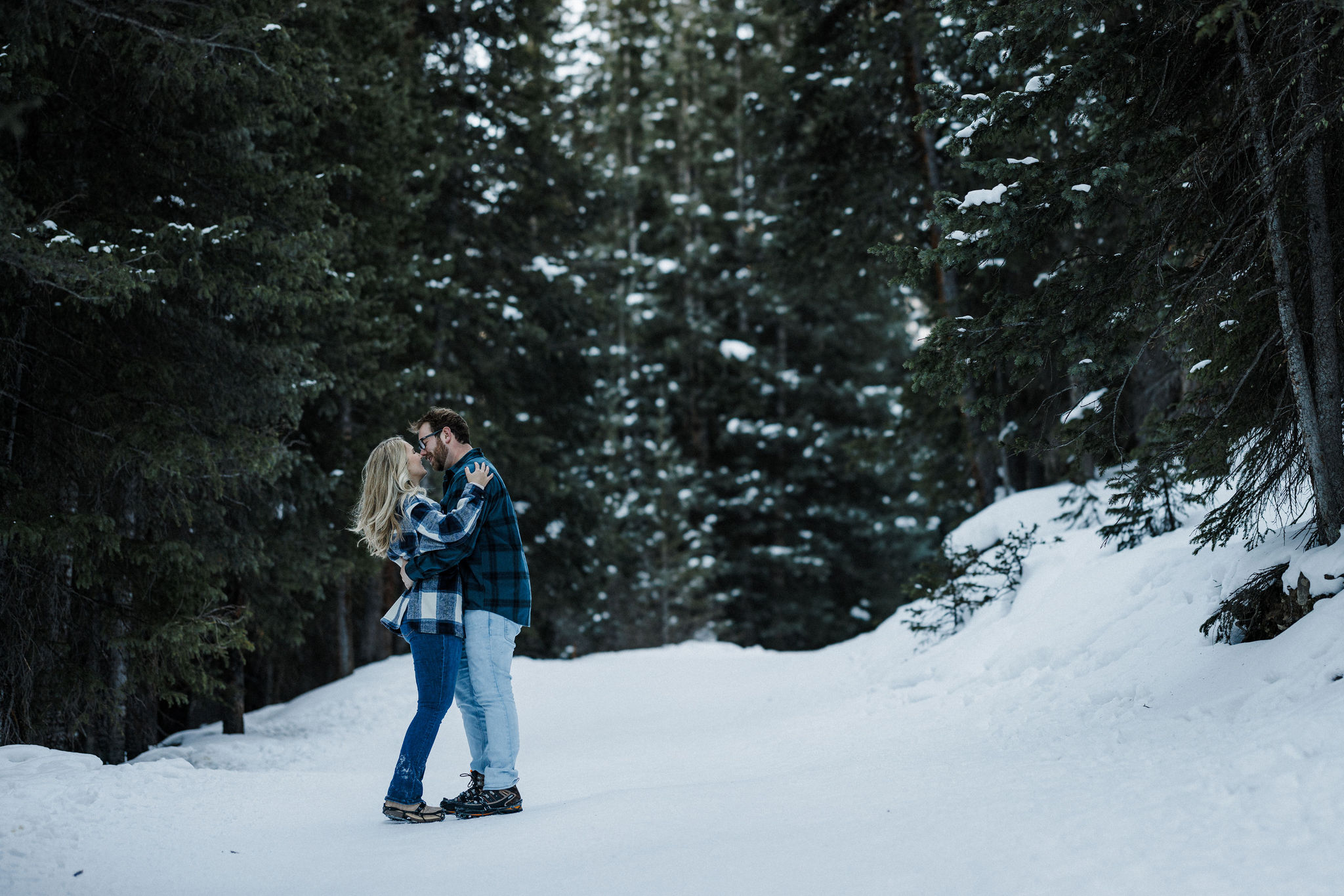 engaged couple kisses on snowy trail.