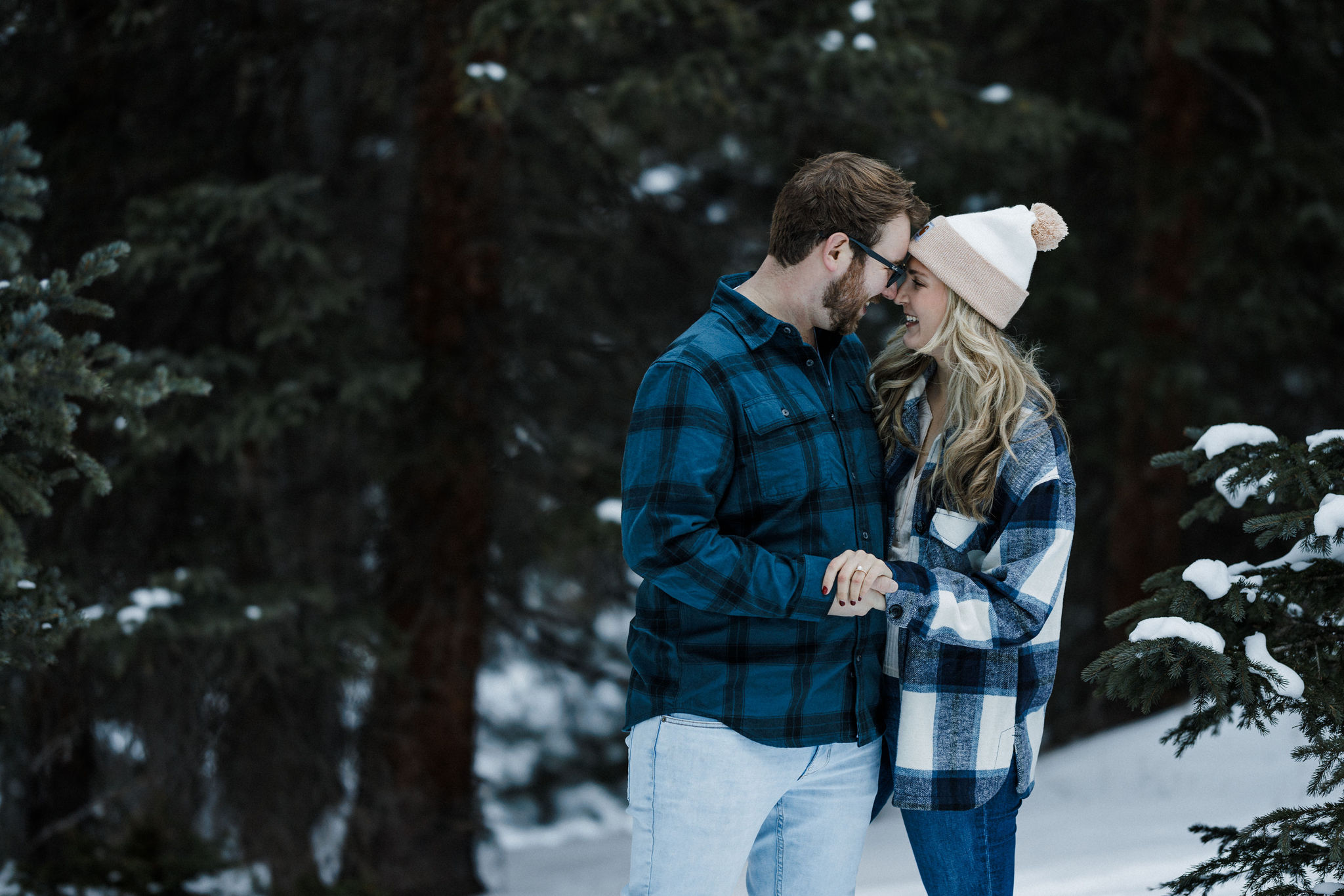 engaged couple smiles head to head during a snowy engagement photo shoot.