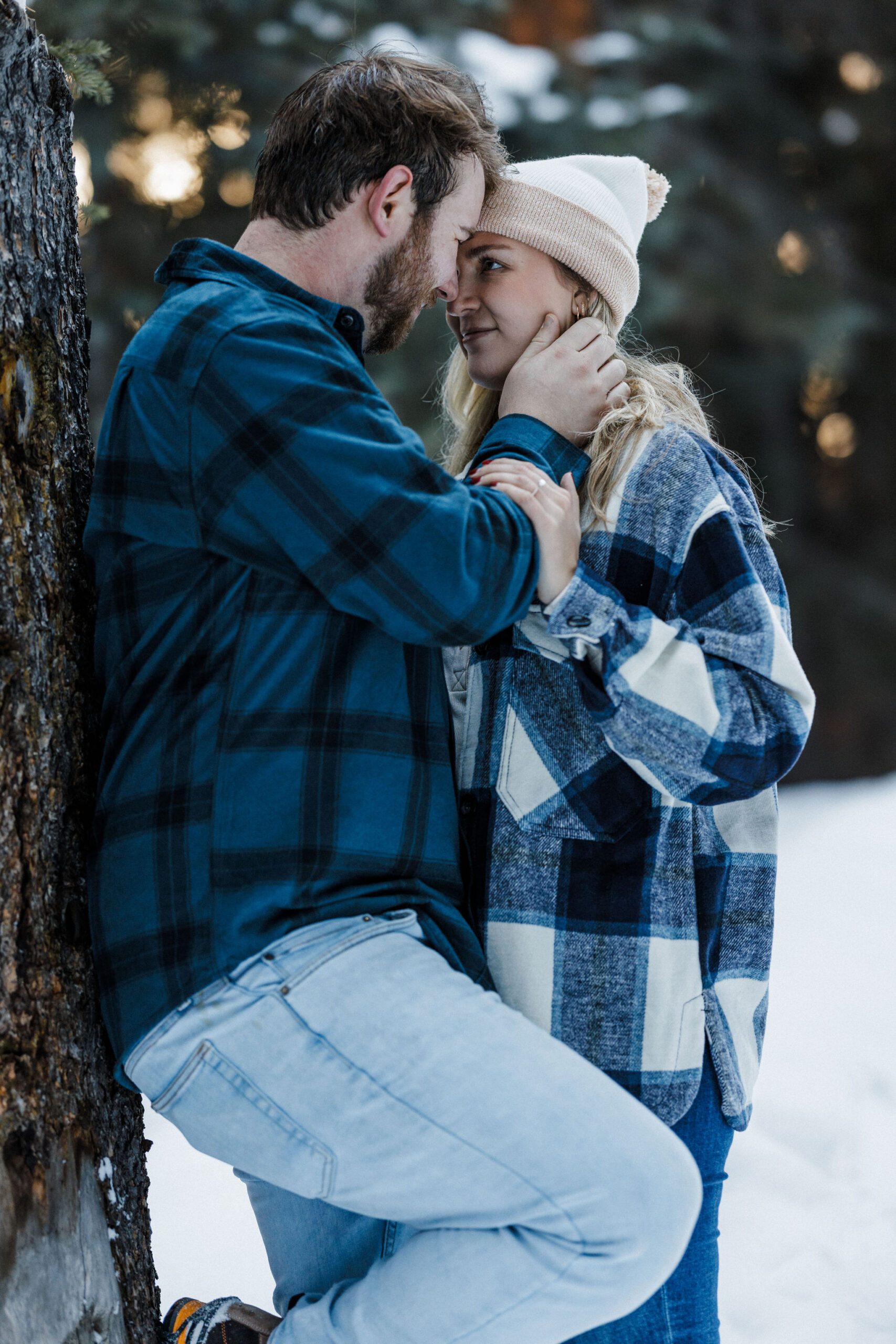 engaged couple leans against a tree head to head during winter engagement photos