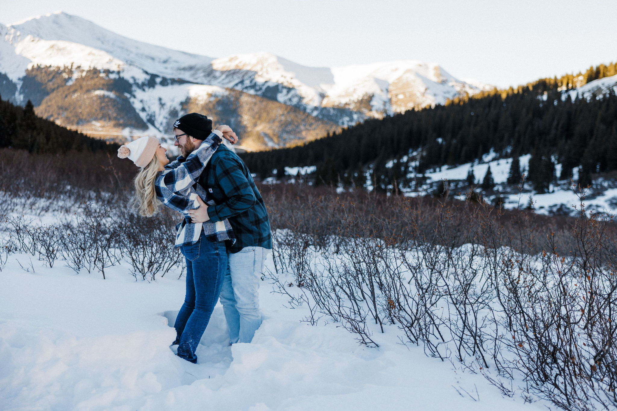engaged couple hugs and smiles in front of the colorado mountains during engagement photos.
