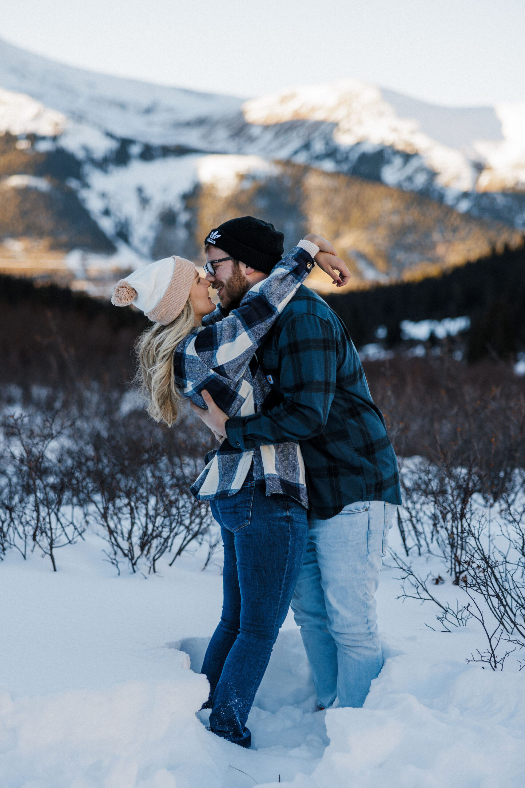 engaged couple embraces wuhile standing in the snow during winter engagement photo shoot.