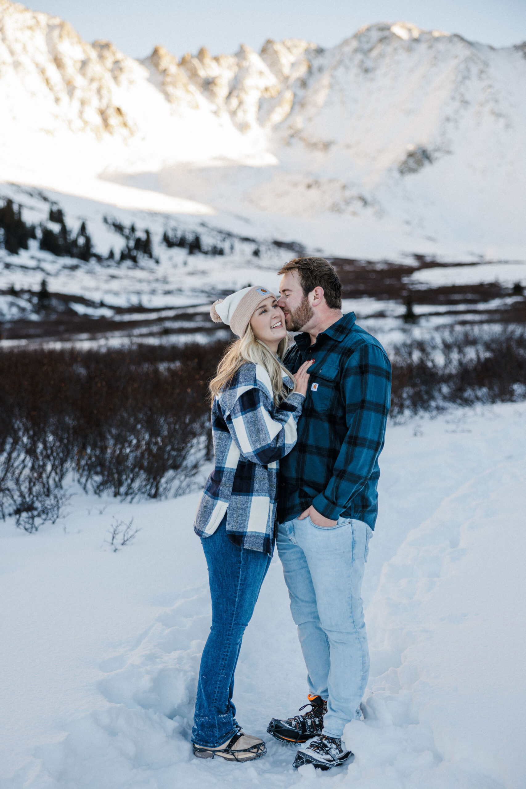 man kisses womans cheek during winter engagement photos in colorado.