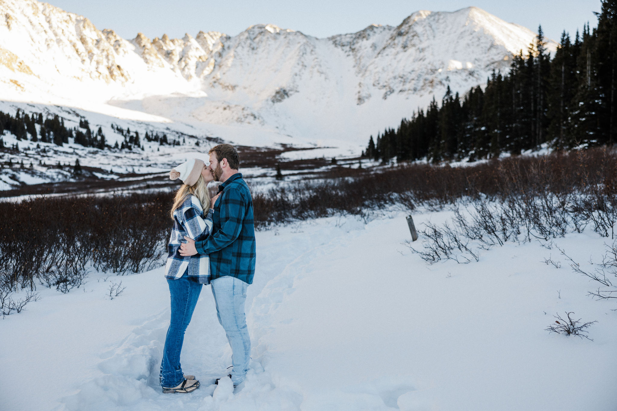 engaged couple kisses in front of the snowy colorado mountains.