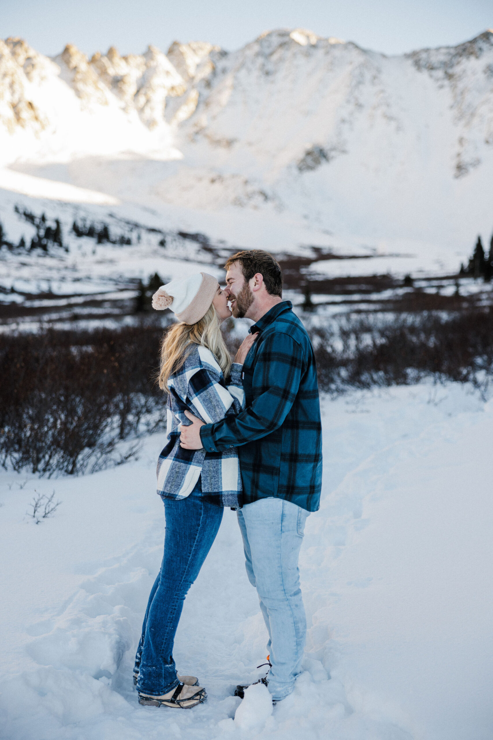 engaged couple kiss in front of the snowy colorado mountains.