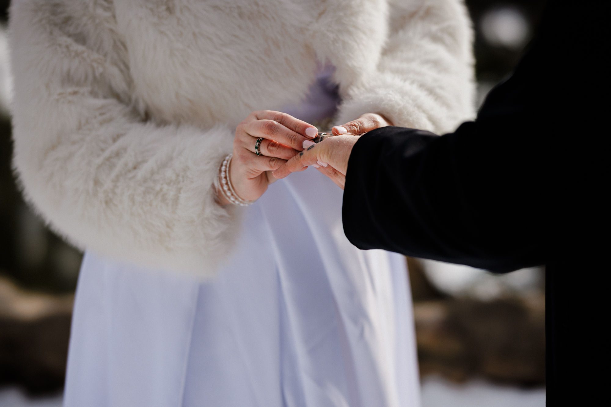 bride in winter wedding dress puts wedding band on husband's finger