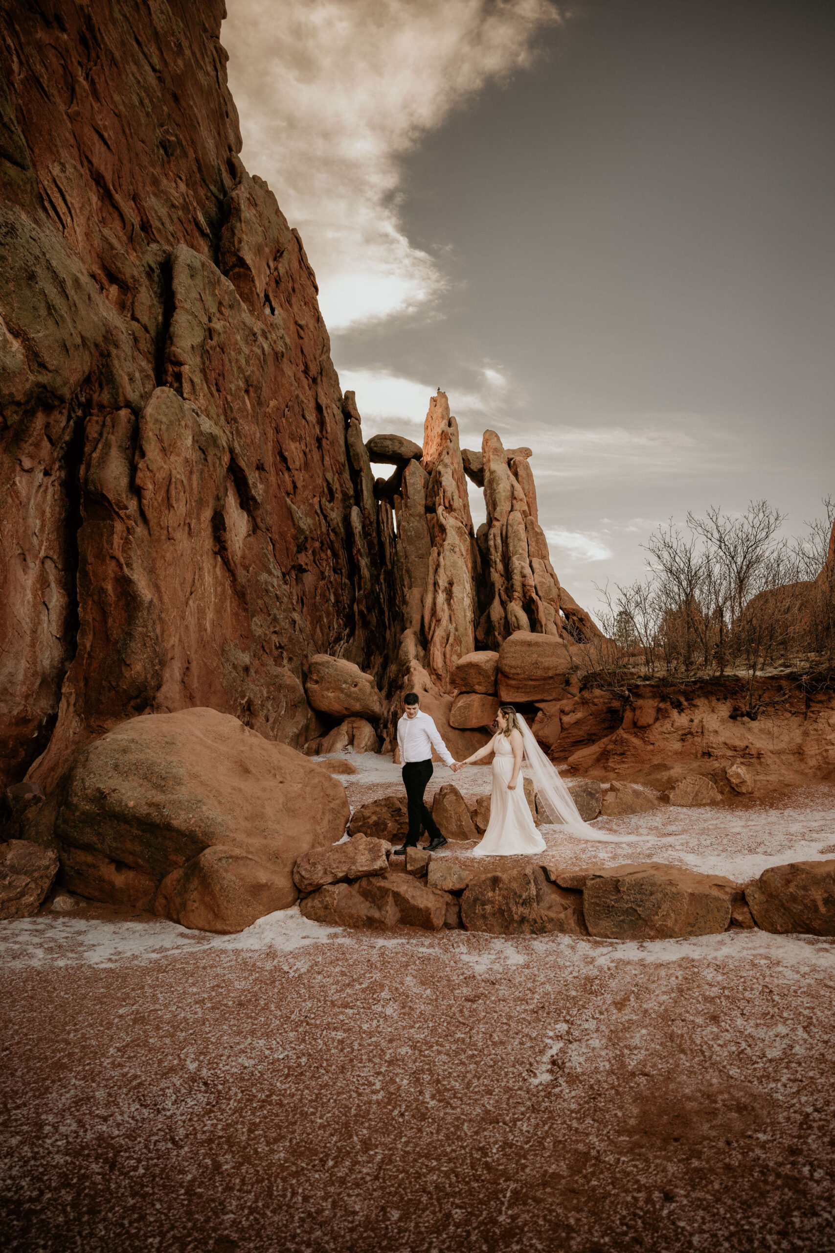 bride and groom hold hands and walk through giant red rocks during winter elopement at garden of the gods