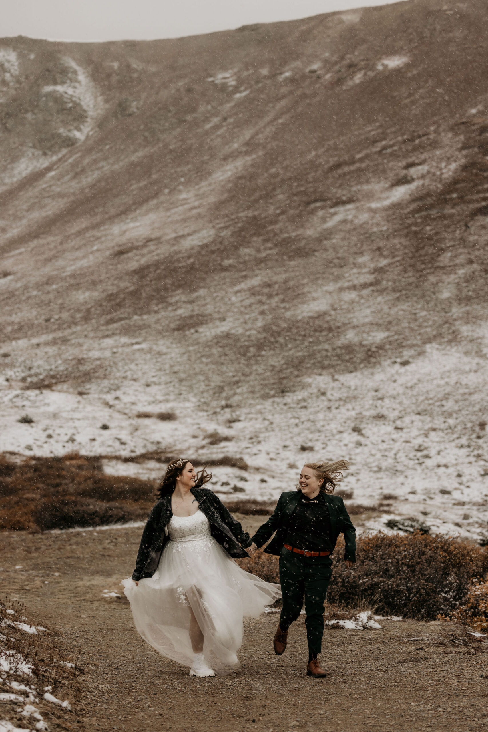 two brides run through path in the winter in colorado.