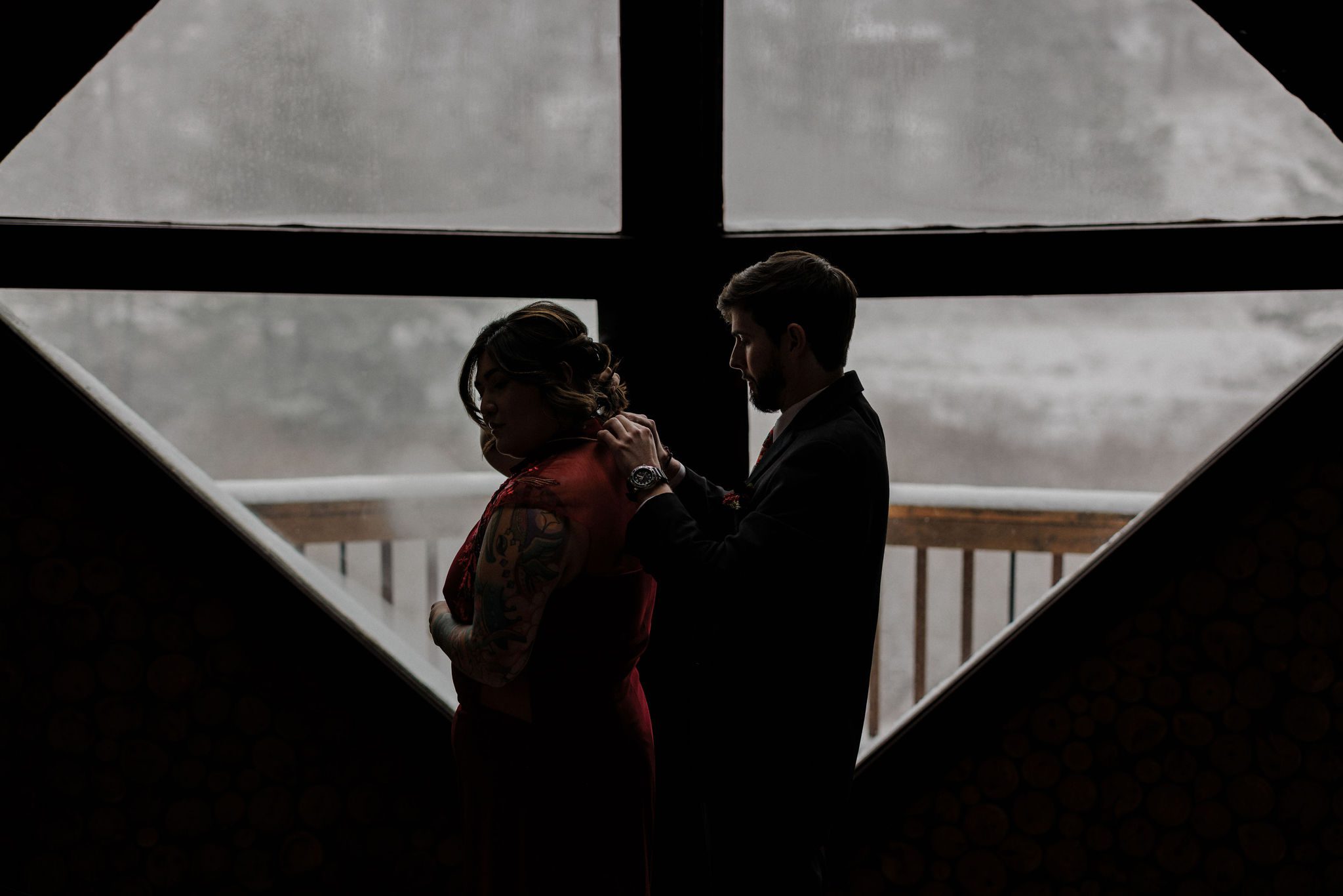 groom puts necklace on bride in front of snowy window at airbnb venue