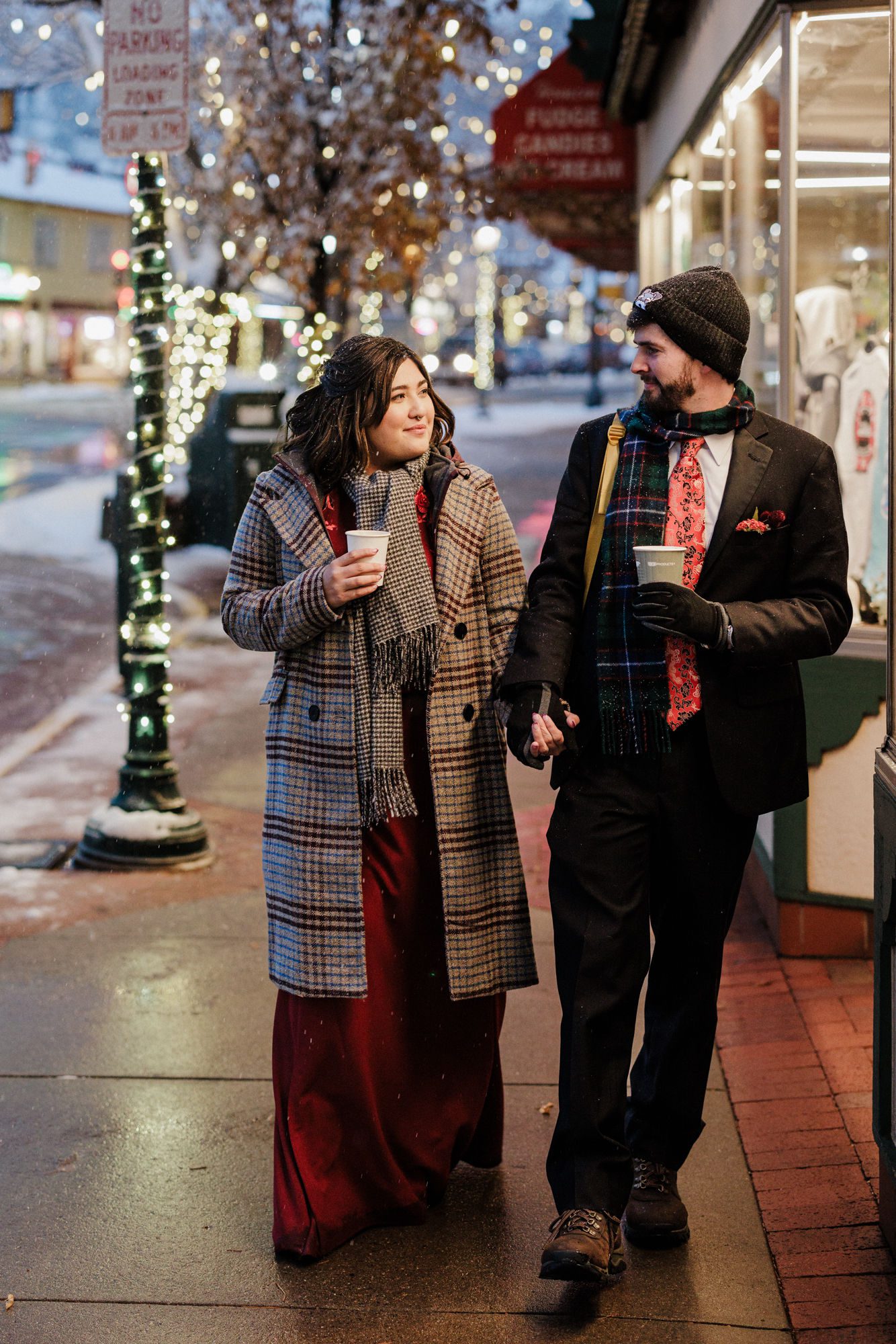 bride in winter elopement dress and groom hold hot chocolate and walk down streen in estes park colorado