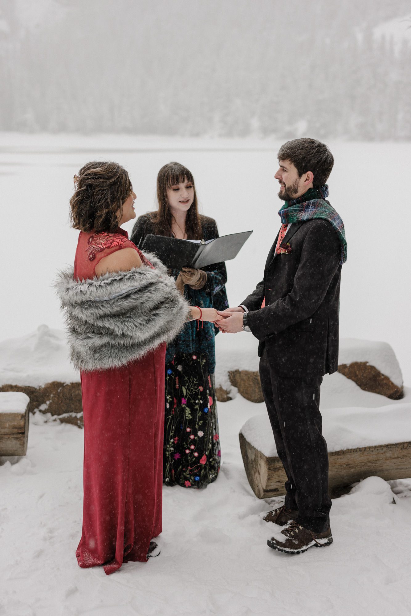 bride and groom hold hands as officiant talks during their winter elopement in colorado