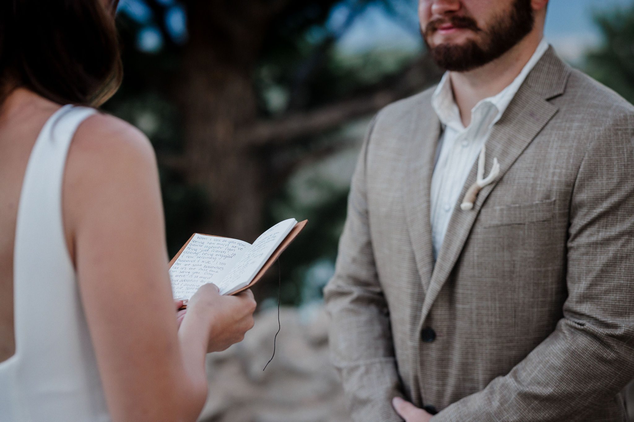 during  self-solemnization elopement in colorado, bride holds wedding vows book and speaks to groom