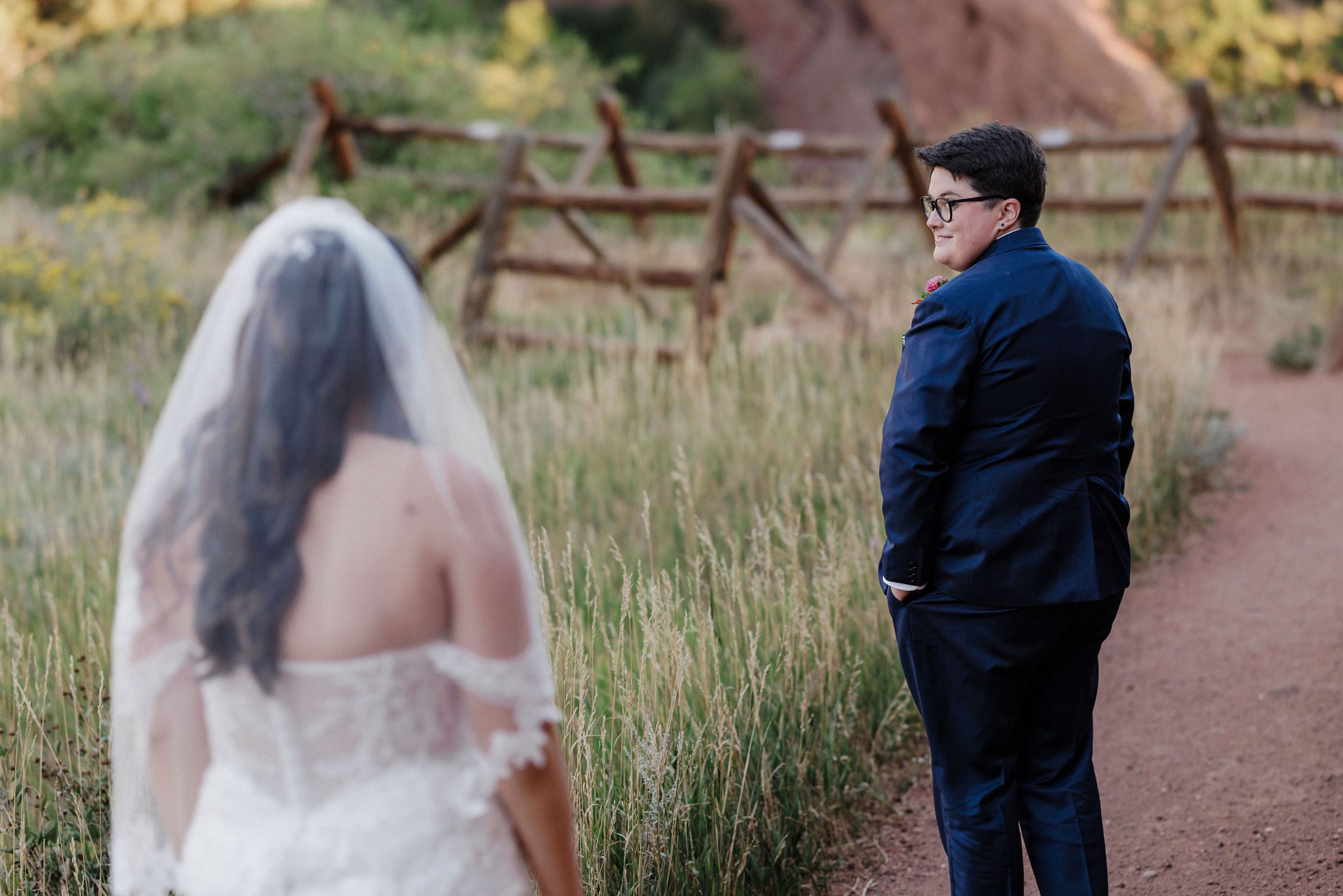 bride in suit turns and looks at bride in dress who is behind her for their first look for their elopement