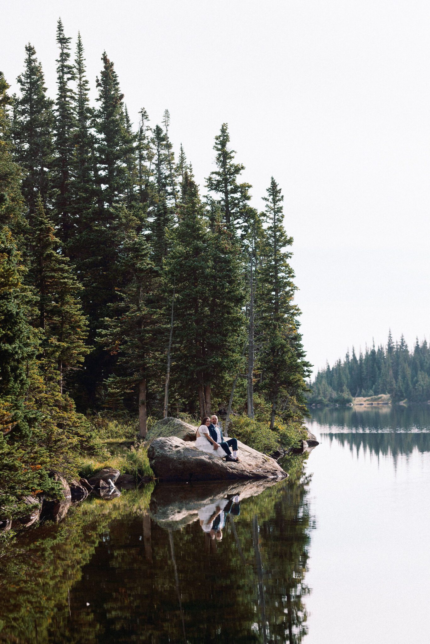 bride and groom sit on rock that is in a mountain lake and look at colorado elopement photographer