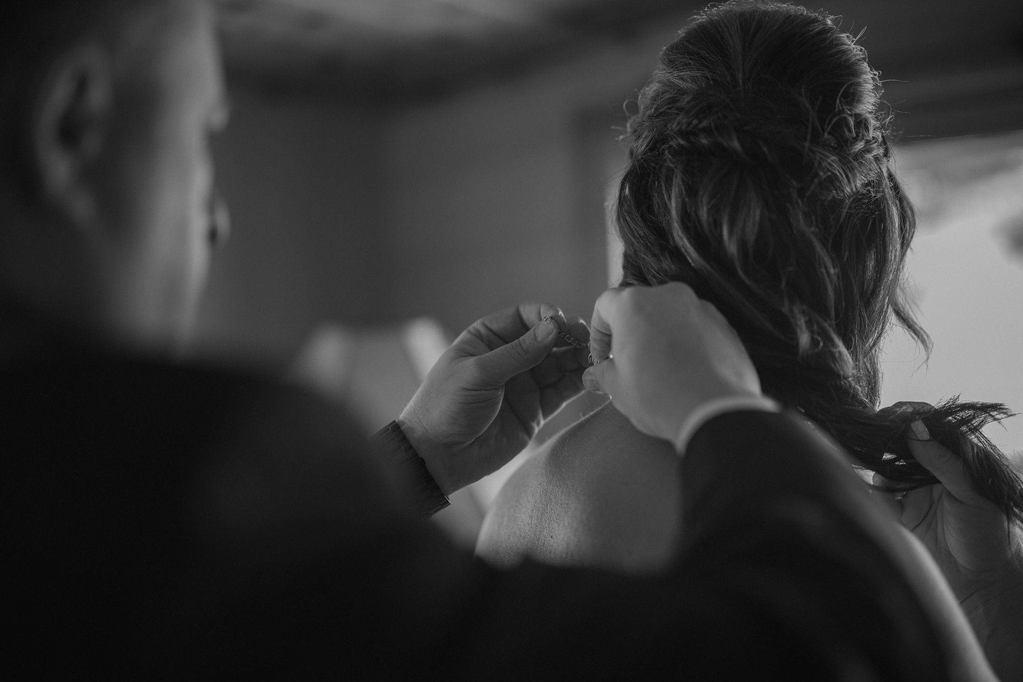 groom puts necklace on bride while getting ready
