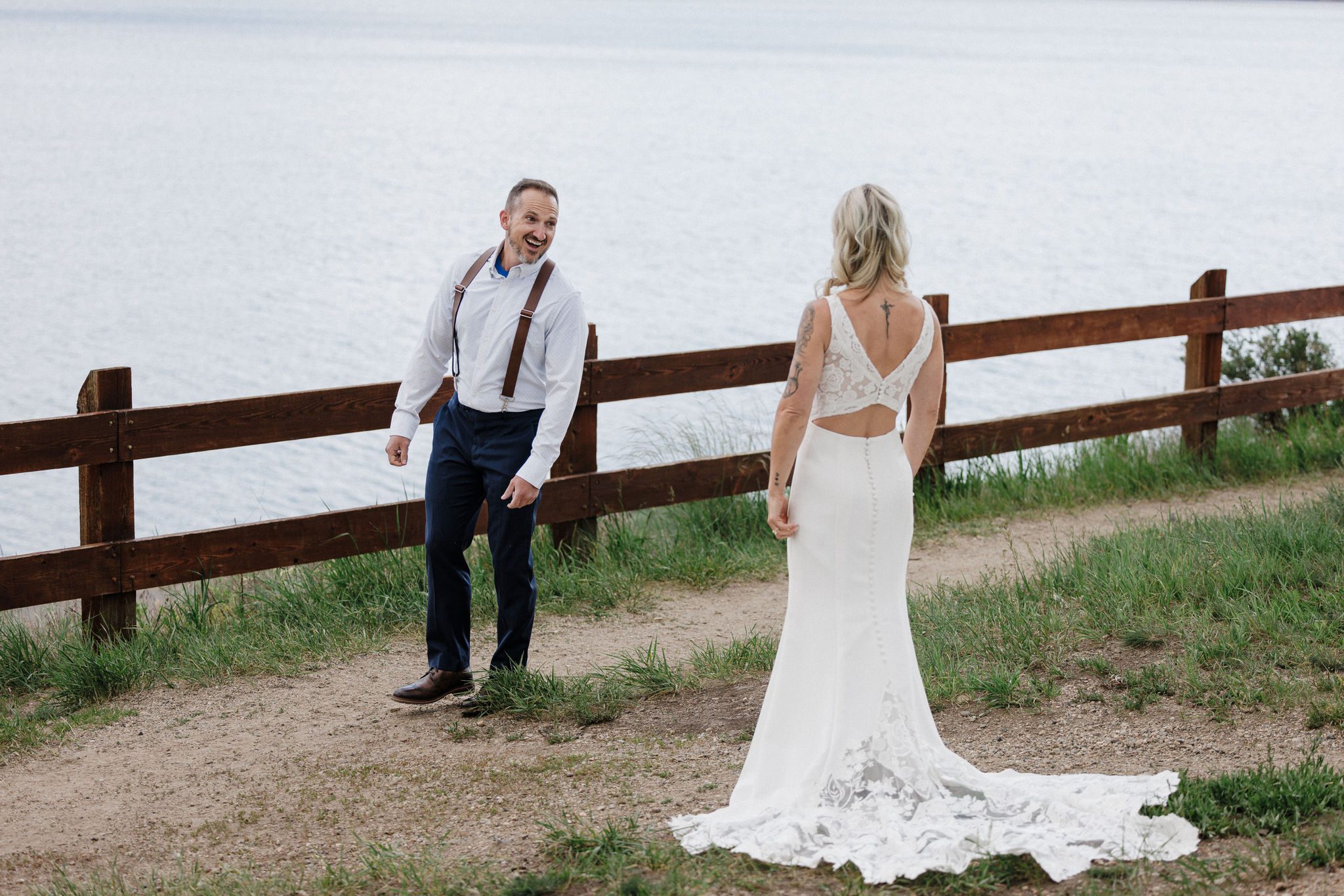 bride stands behind groom as he turns around and smiles during their first look idea for their wedding