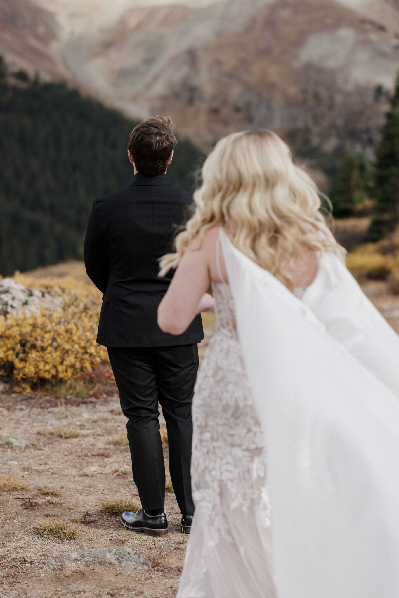 bride stands behind groom before their wedding day first look idea of going in the mountains