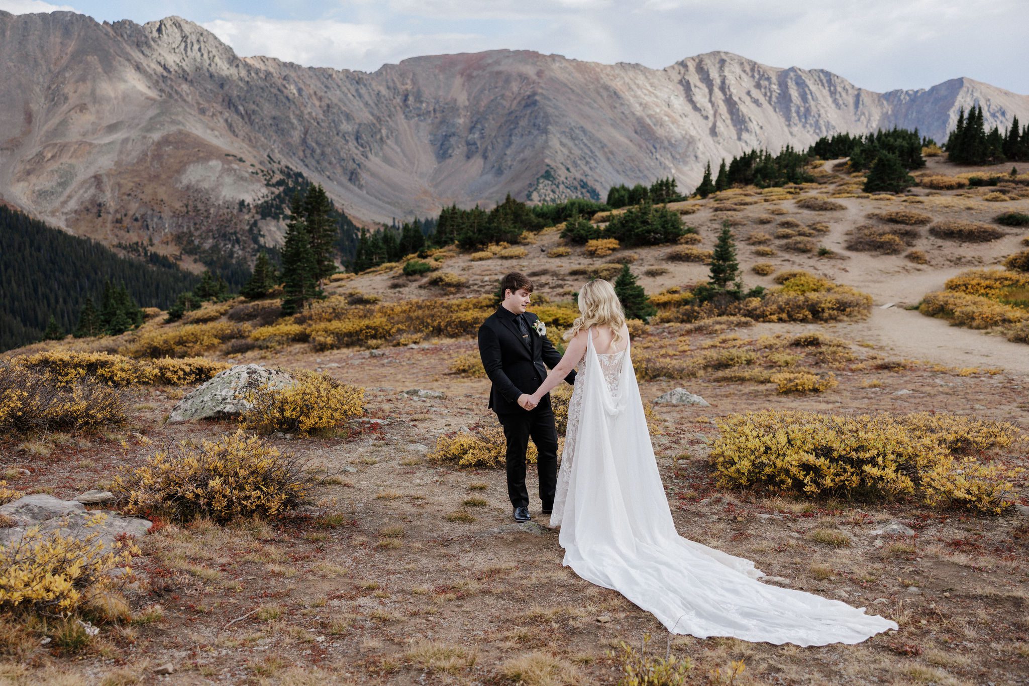 bride and groom stand in the colorado mountains and hold hands and face each other after their wedding day first look