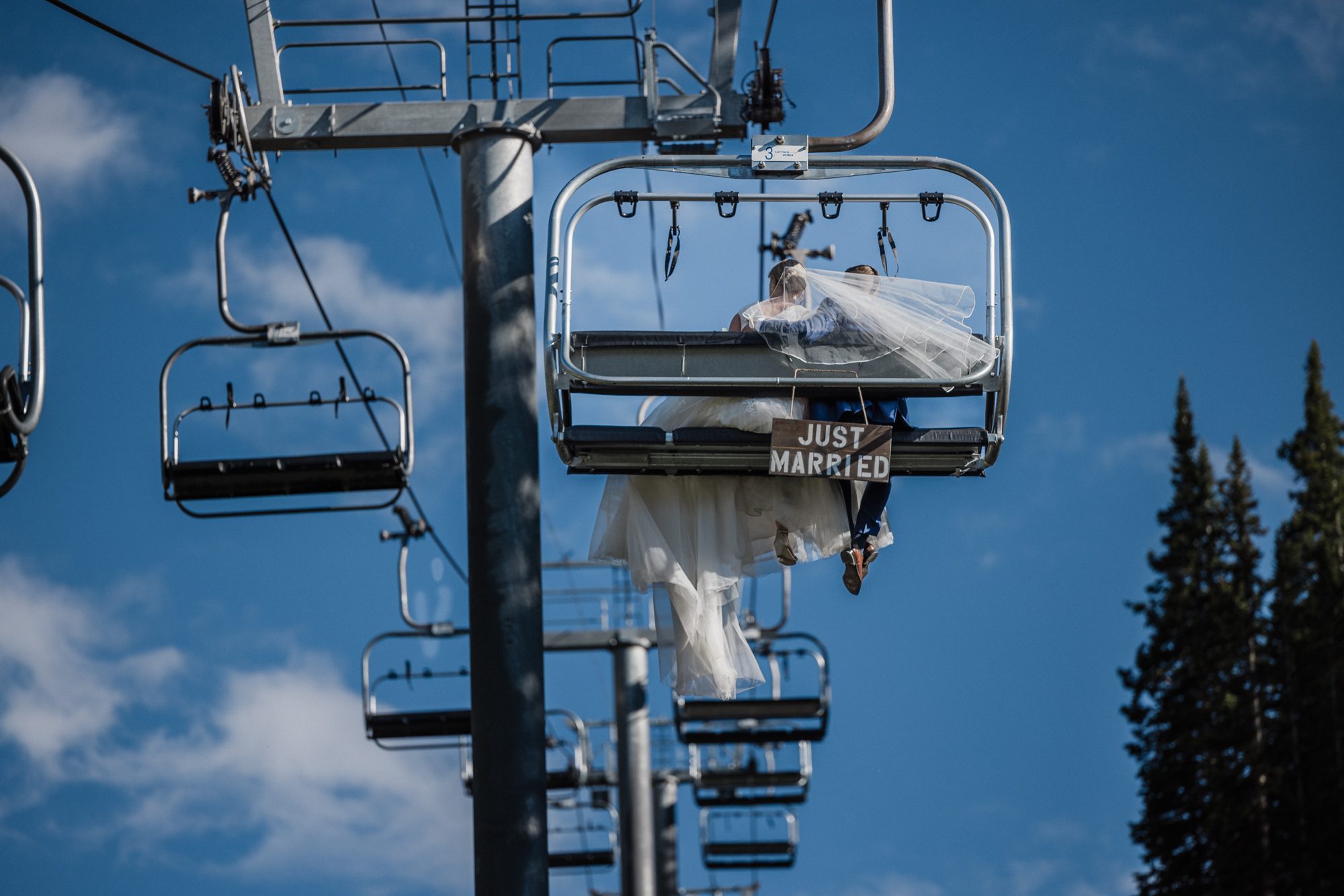 bride and groom ride on ski lift as their second wedding idea, with a sign on the back saying 'just married'