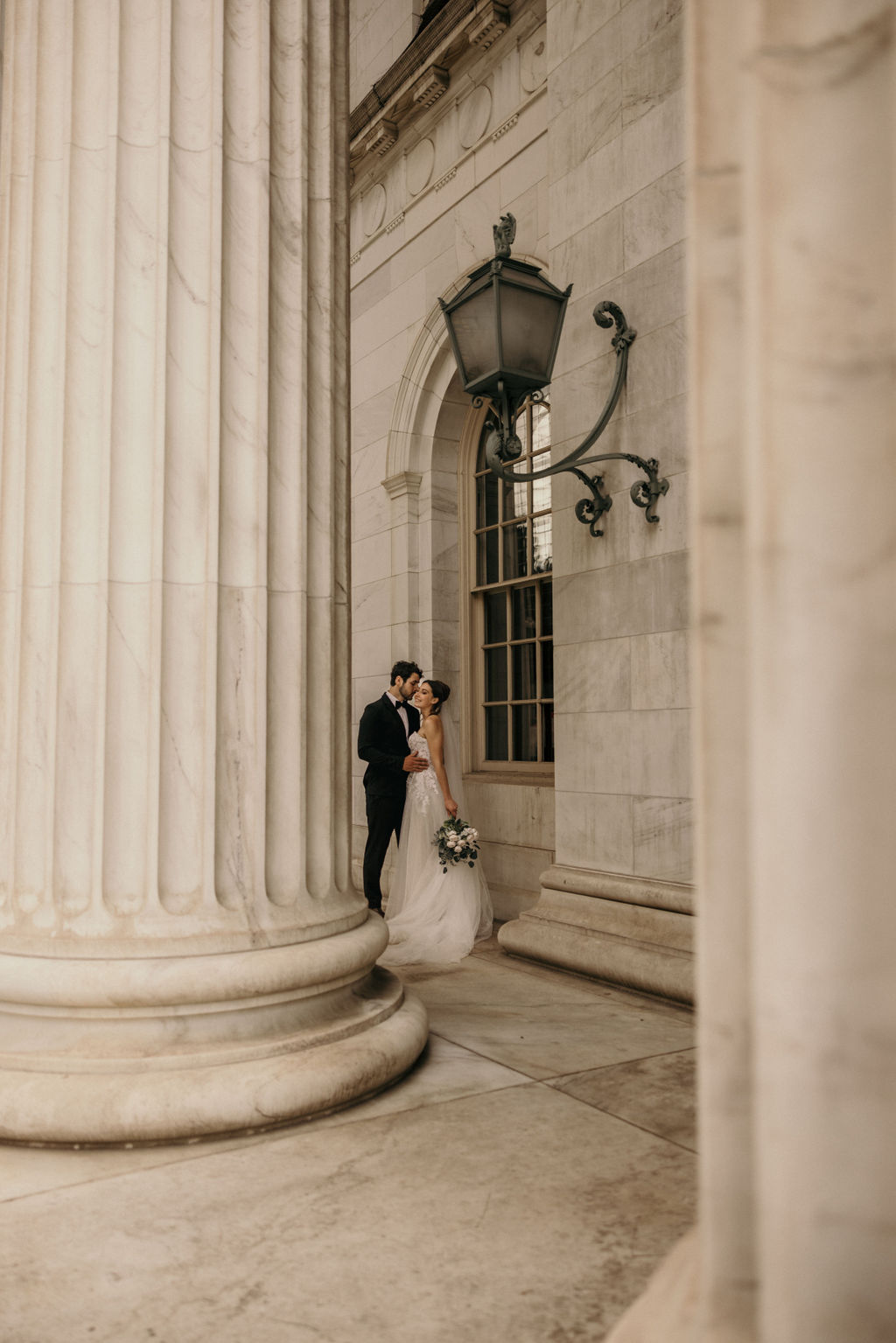 bride and groom stand by marble columns of the courthouse during downtown denver elopement.