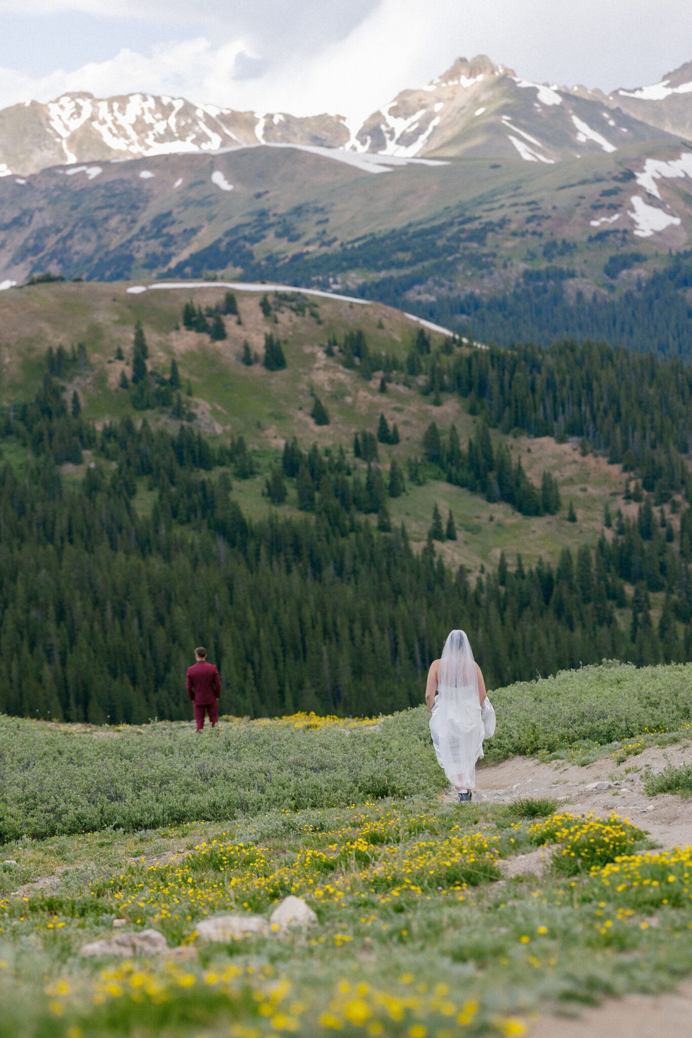bride walks down a mountain with wildflowers during their wedding day first look. they got the adventure colorado elopement package.