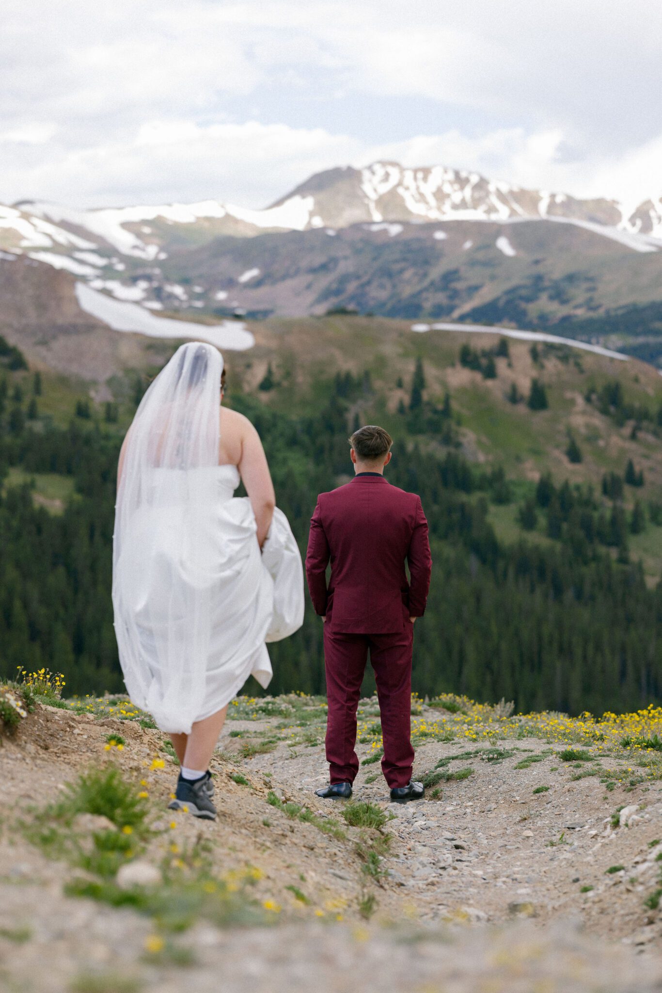 bride stands behind groom that is facing away as a first look idea for their wedding. they are on a train in the colorado mountains